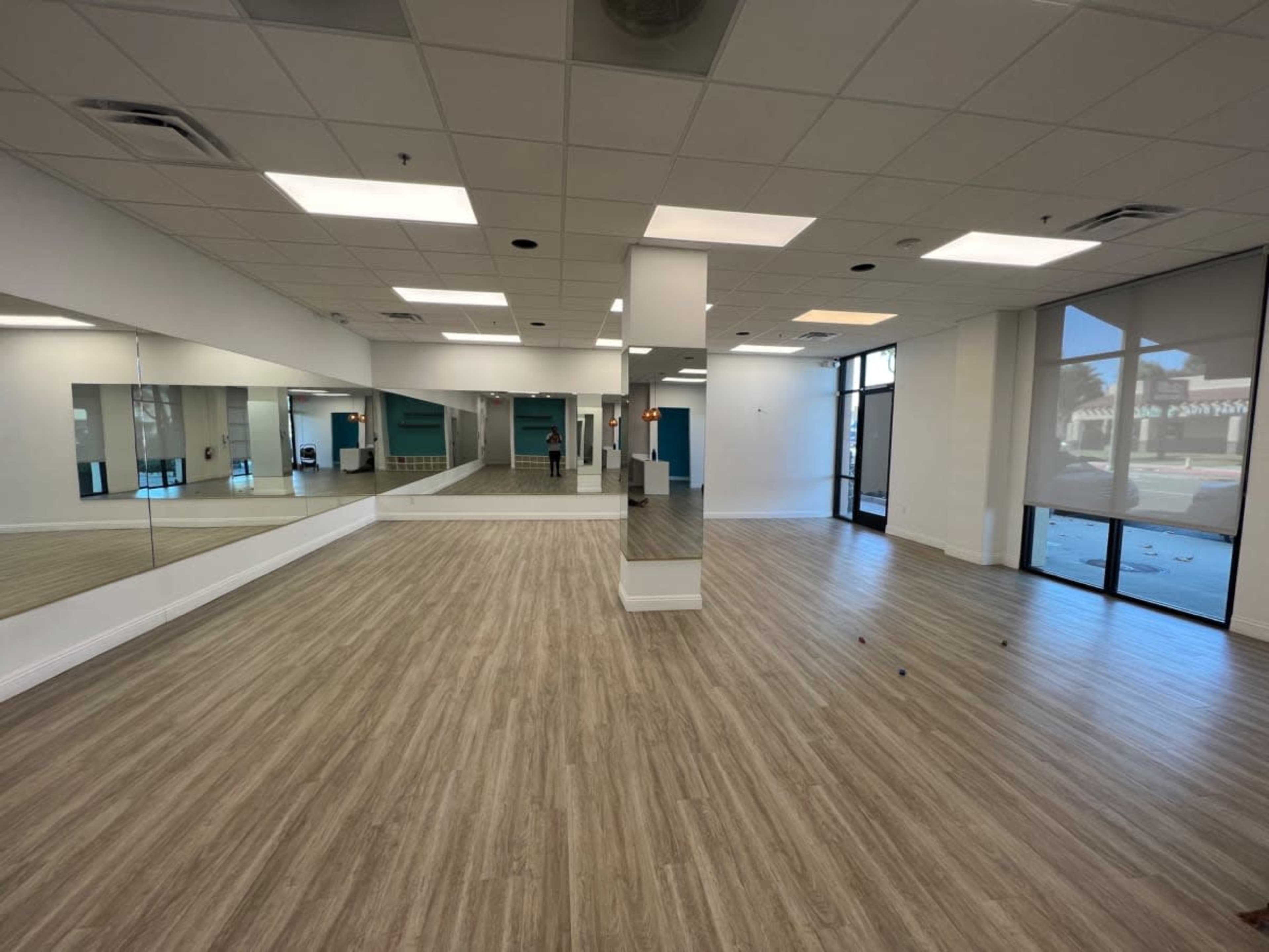 A spacious room with wooden flooring, large mirrors on one wall, and large windows allowing natural light.