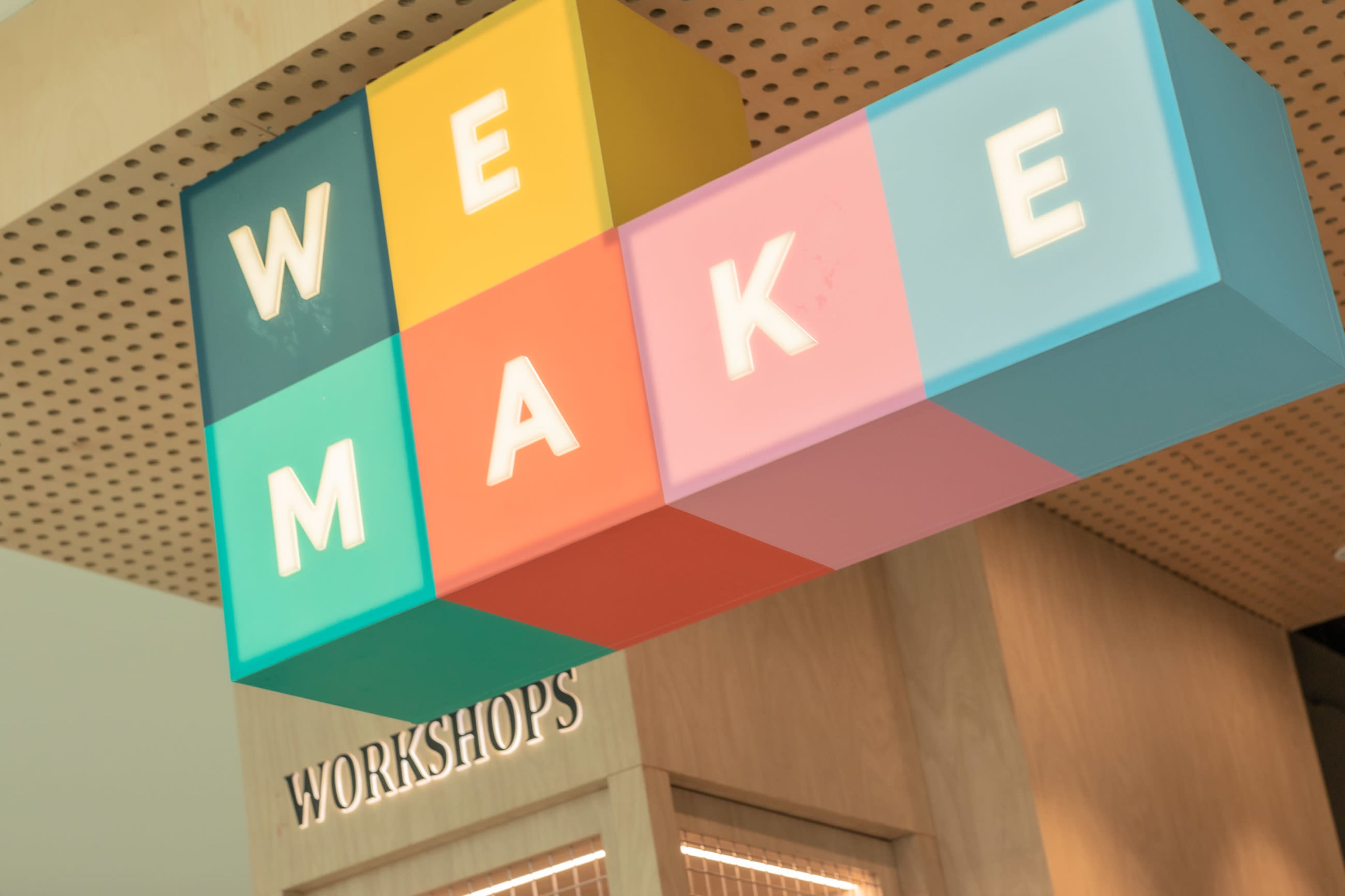 A colorful sign reading "WE MAKE" hangs above a wooden structure labeled "WORKSHOPS."