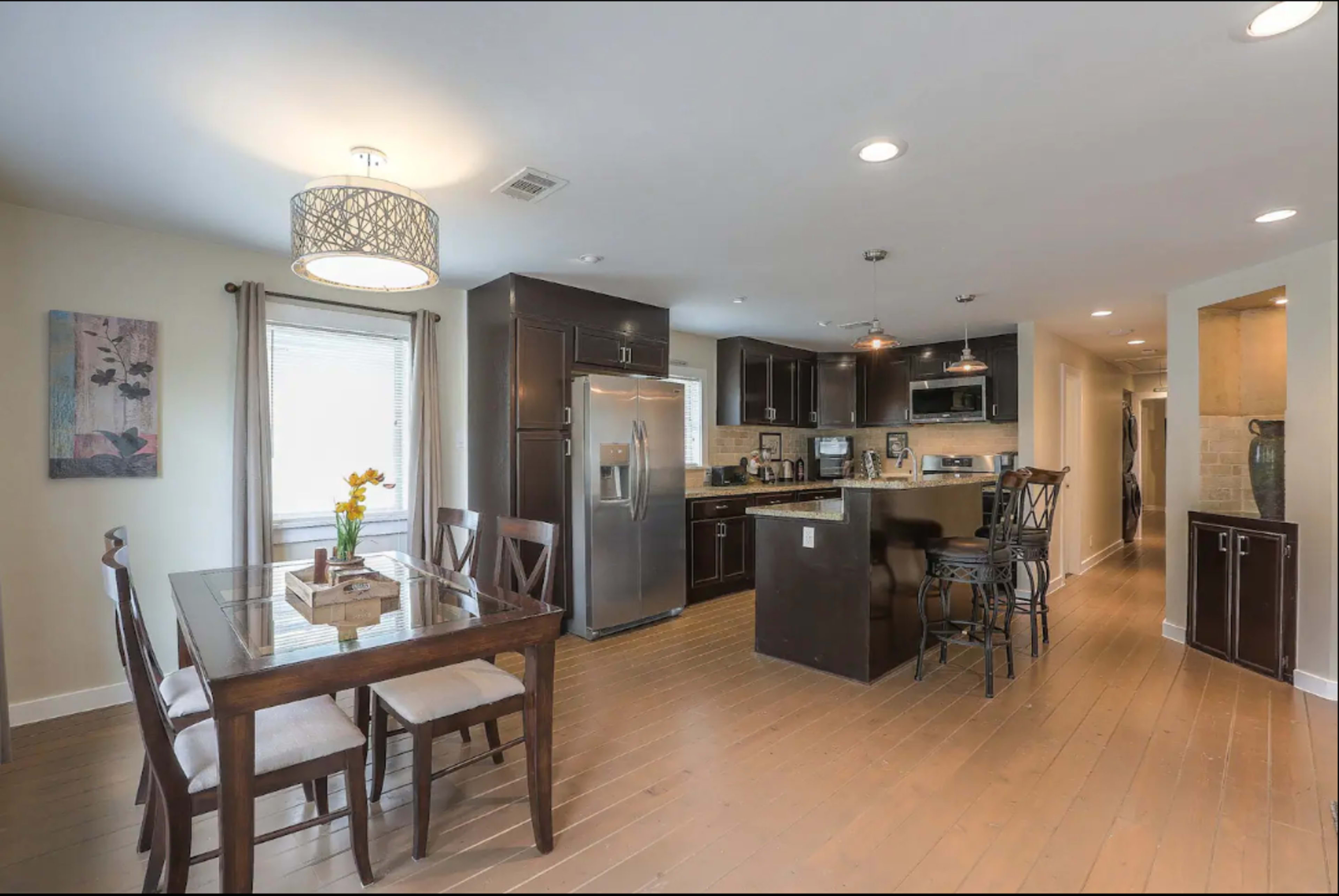 A modern kitchen and dining area featuring dark cabinetry, a stainless steel refrigerator, and a wooden dining table with chairs.