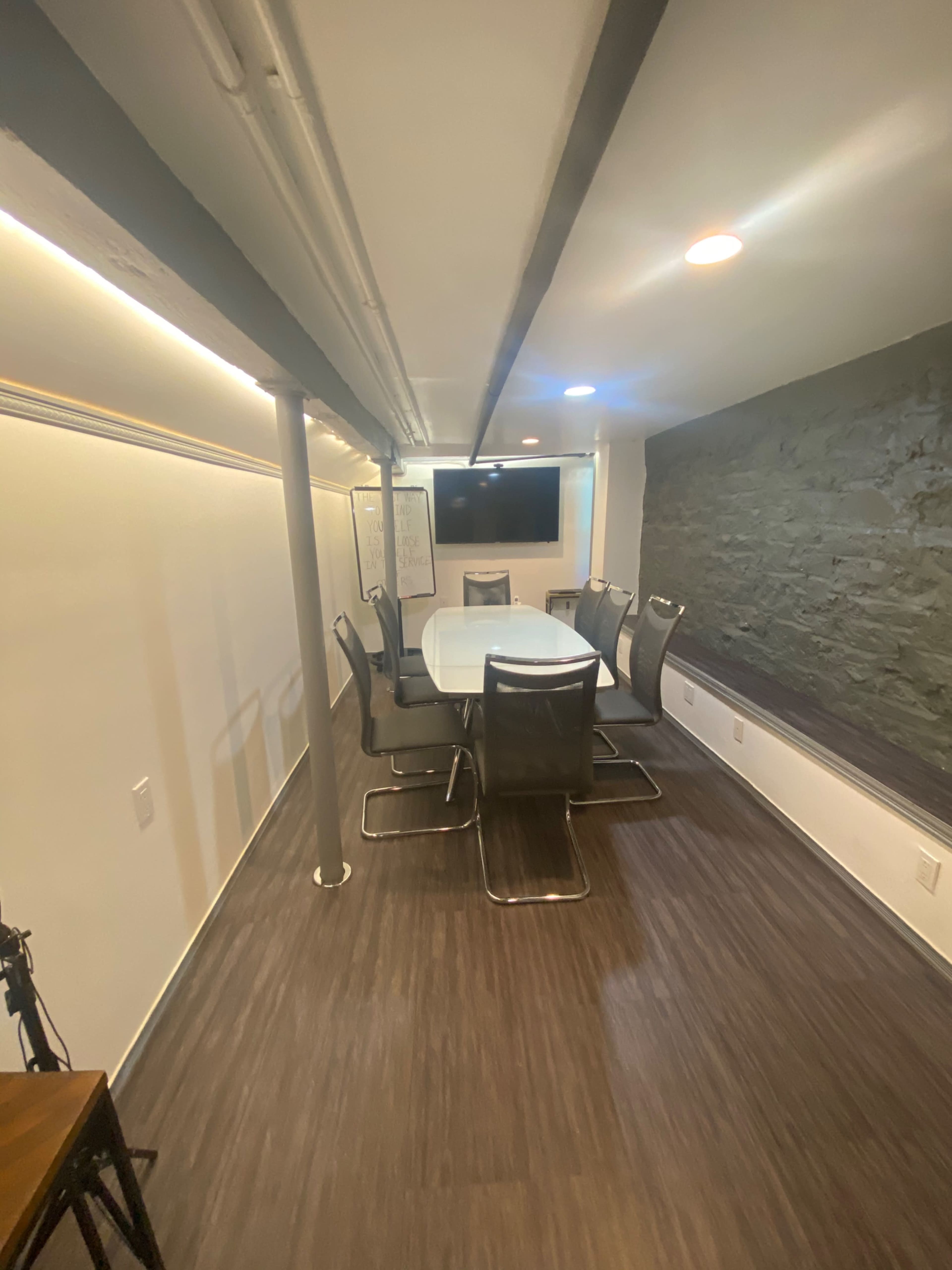 A modern conference room with a large white table, several chairs around it, and a wall-mounted television.