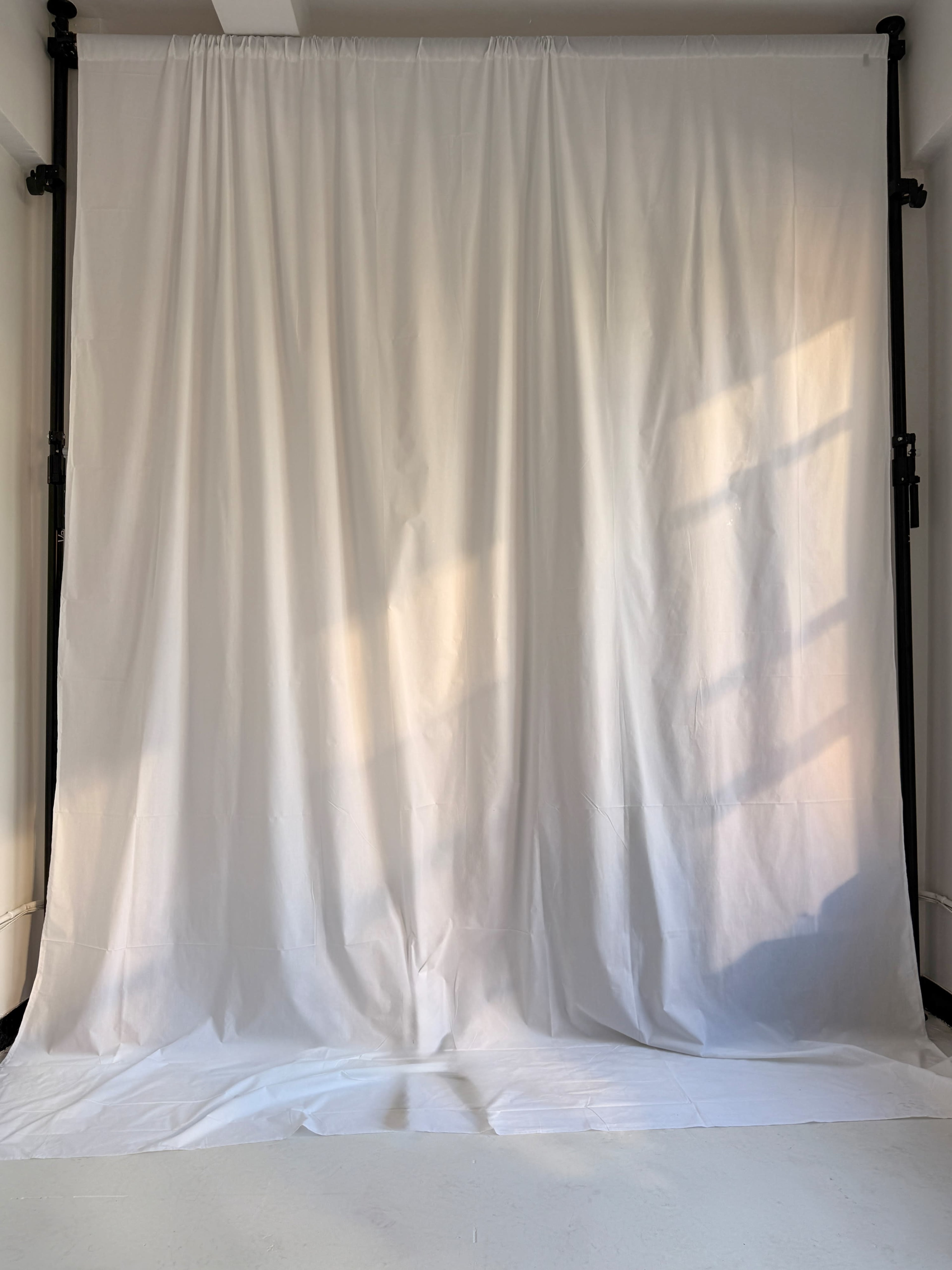 The image shows a plain white backdrop draped on a support frame in a well-lit studio space.