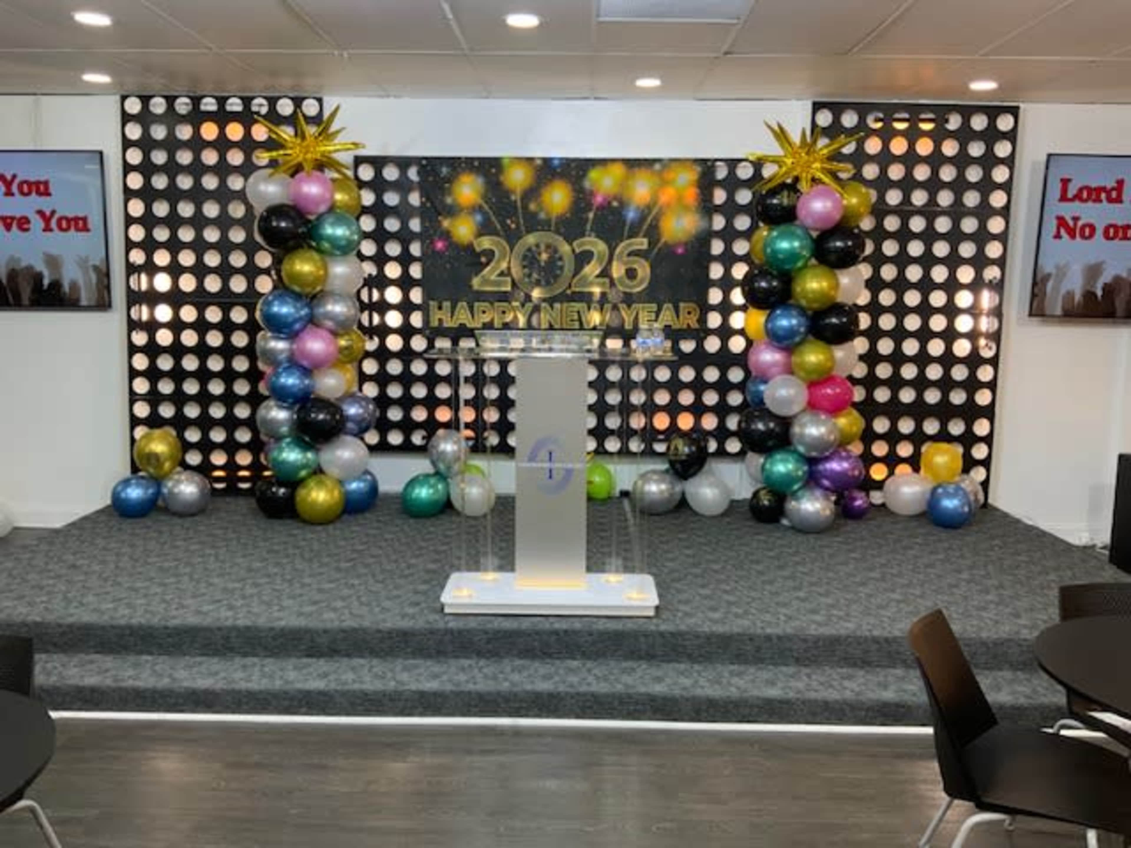 The image shows a stage setup for a New Year celebration, featuring a large "2023 HAPPY NEW YEAR" sign surrounded by colorful balloons and decorative stars.