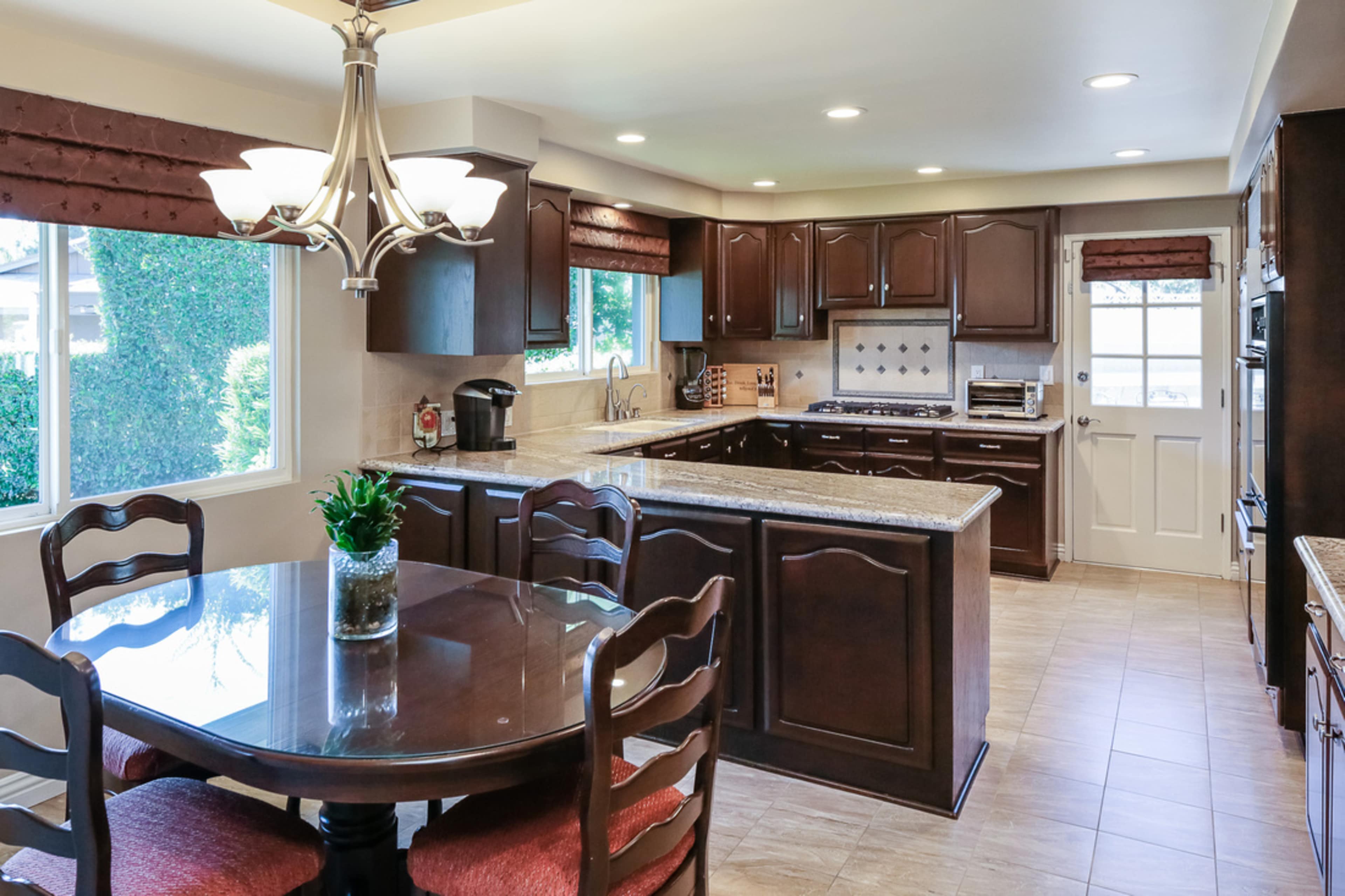 A modern kitchen with dark wooden cabinets, a granite countertop, and a dining table set for four.