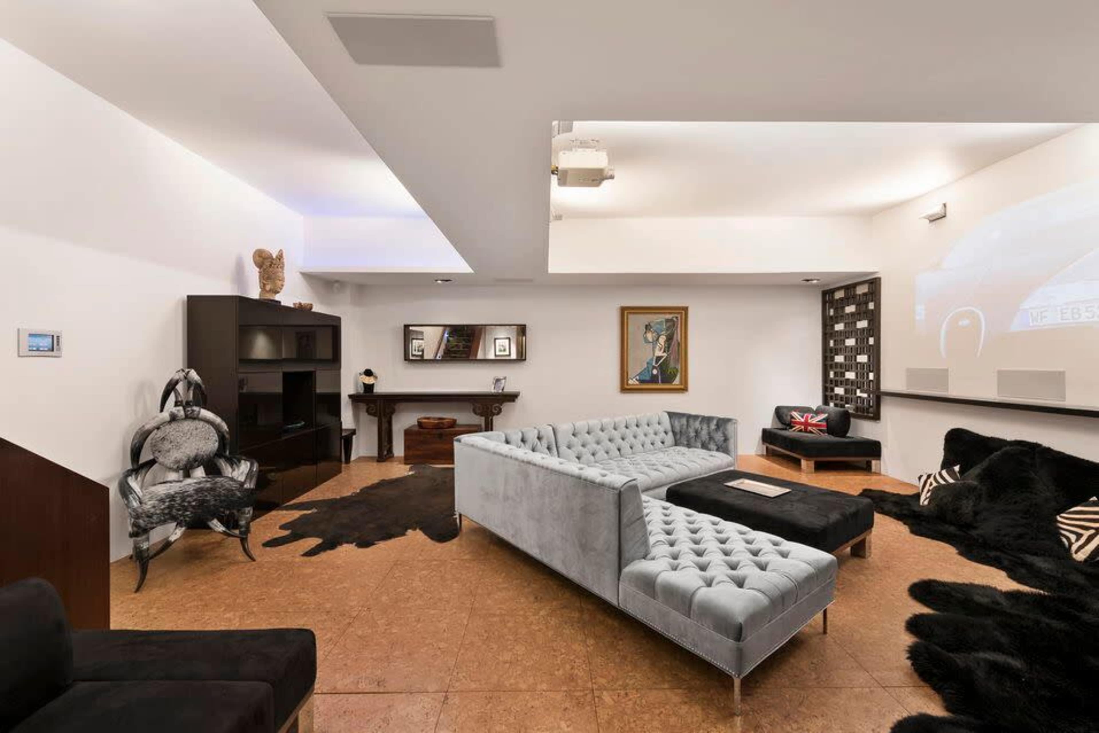 A modern living room with a gray tufted sectional sofa, a black chair, and a large area rug on the cork floor.