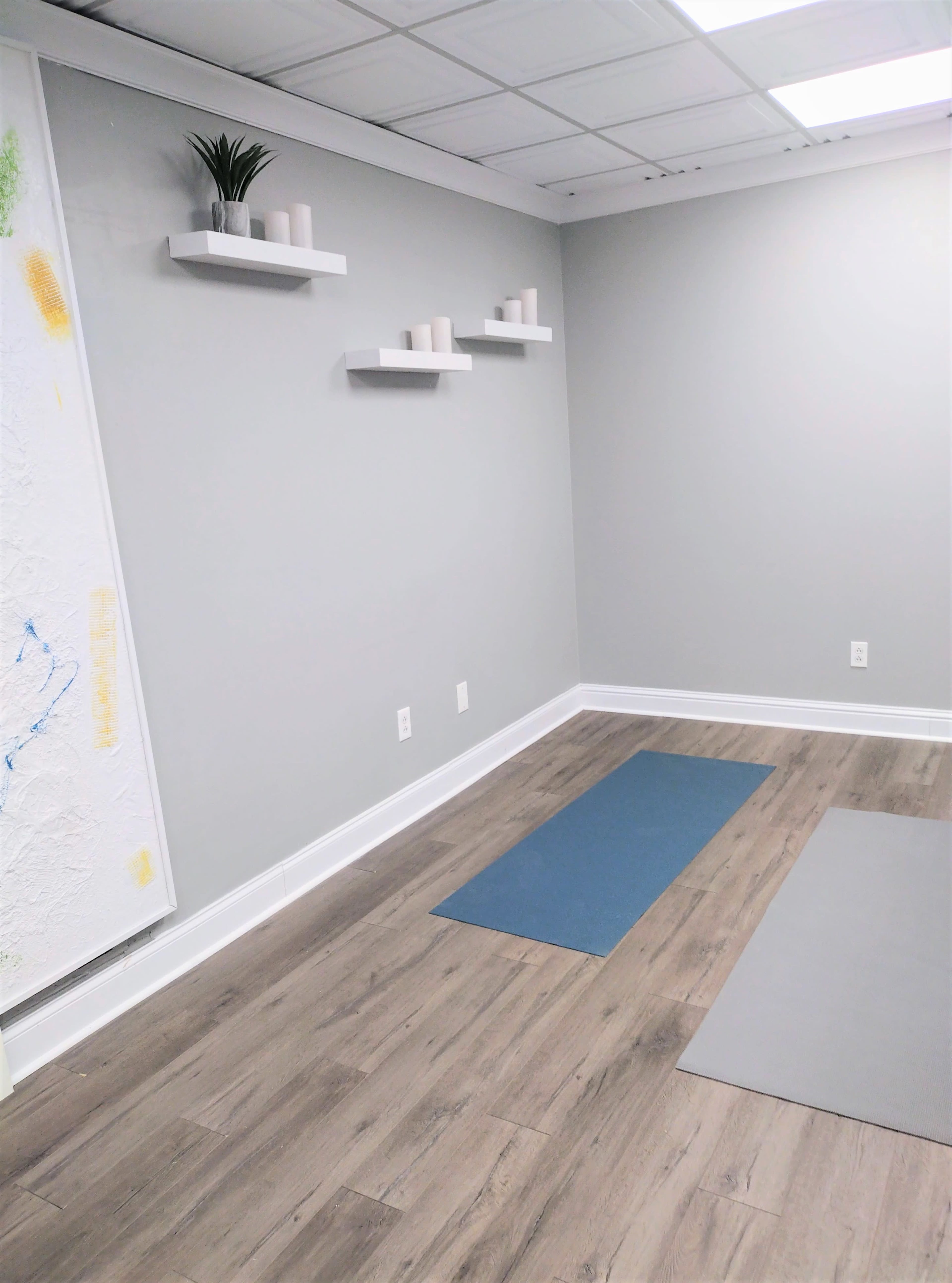 A minimalist room with wooden flooring, three wall-mounted shelves, and two yoga mats on the floor.