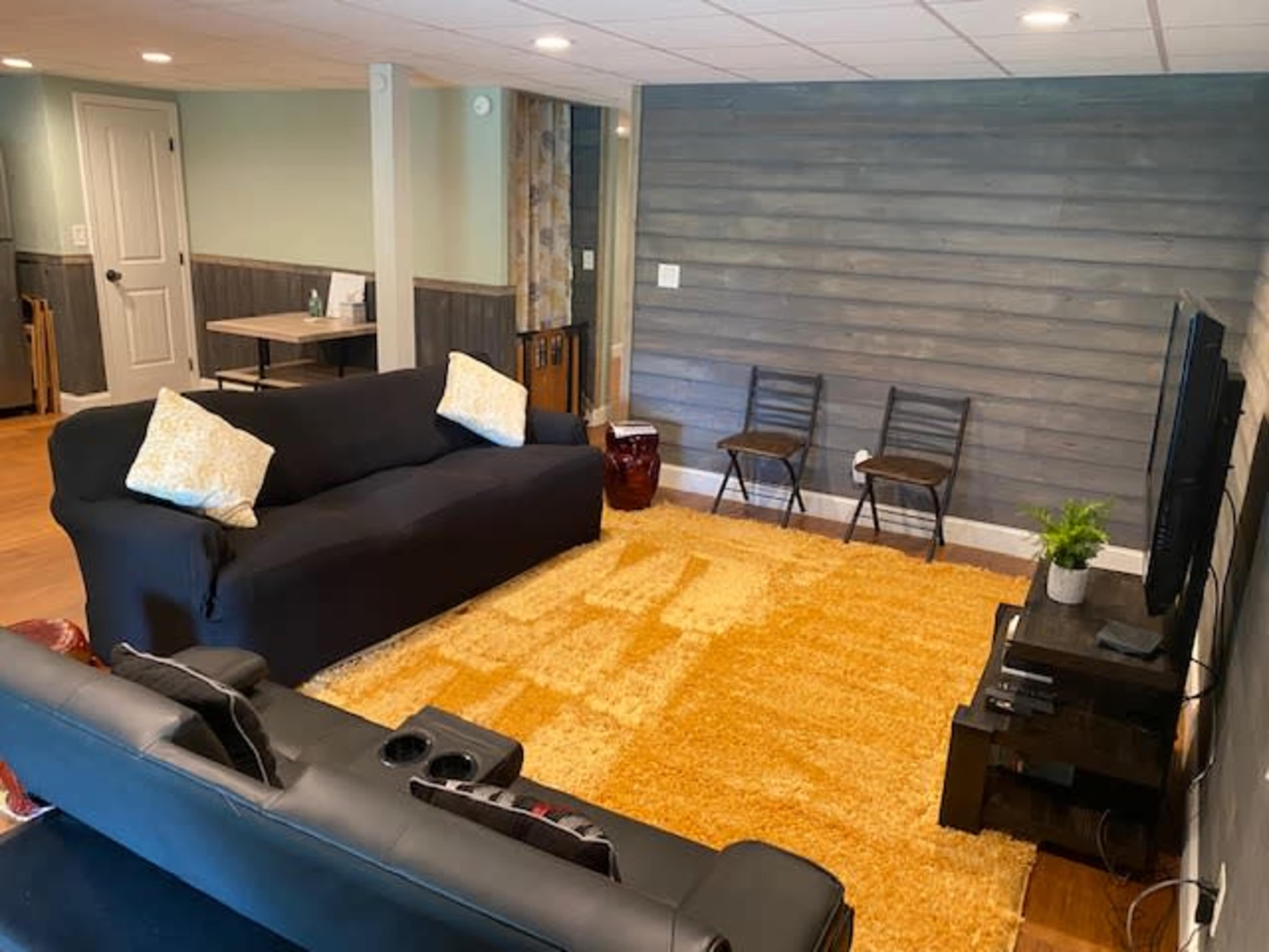 A living room with a black sofa, two chairs, a coffee table, a television, and a large area rug on wooden flooring.