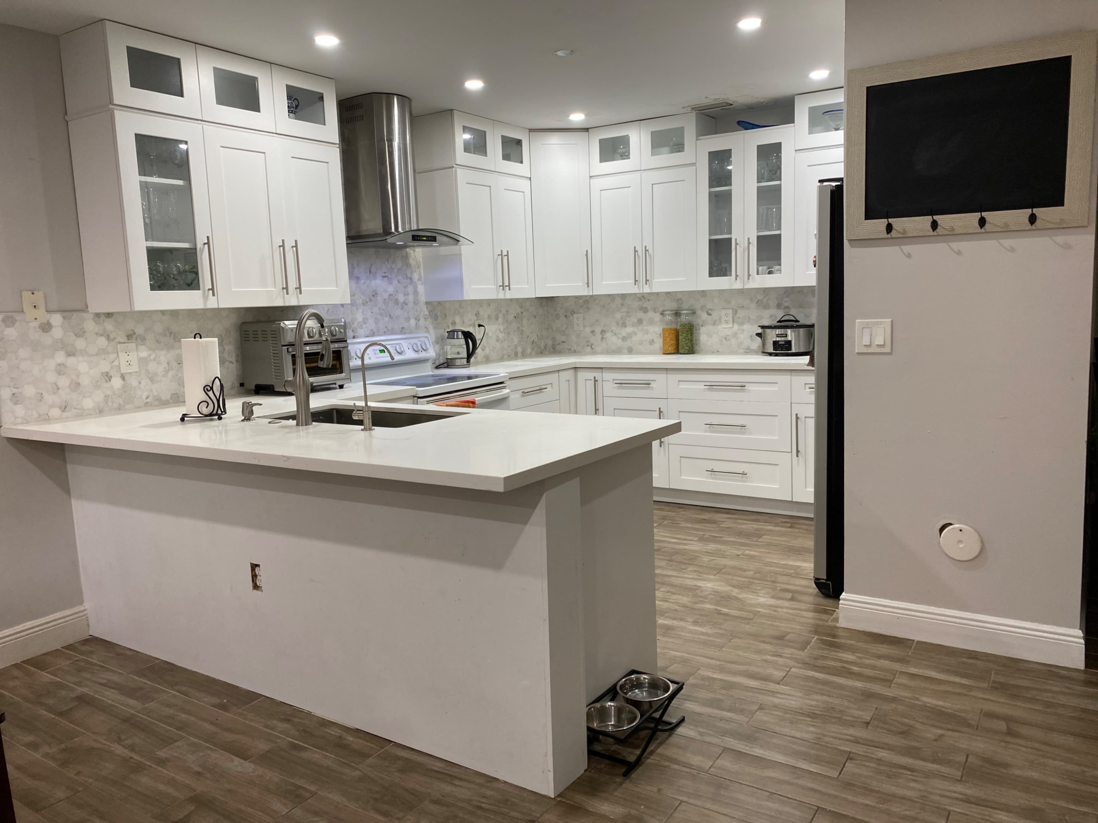 The image shows a modern kitchen with white cabinetry, a central island, and tile flooring.