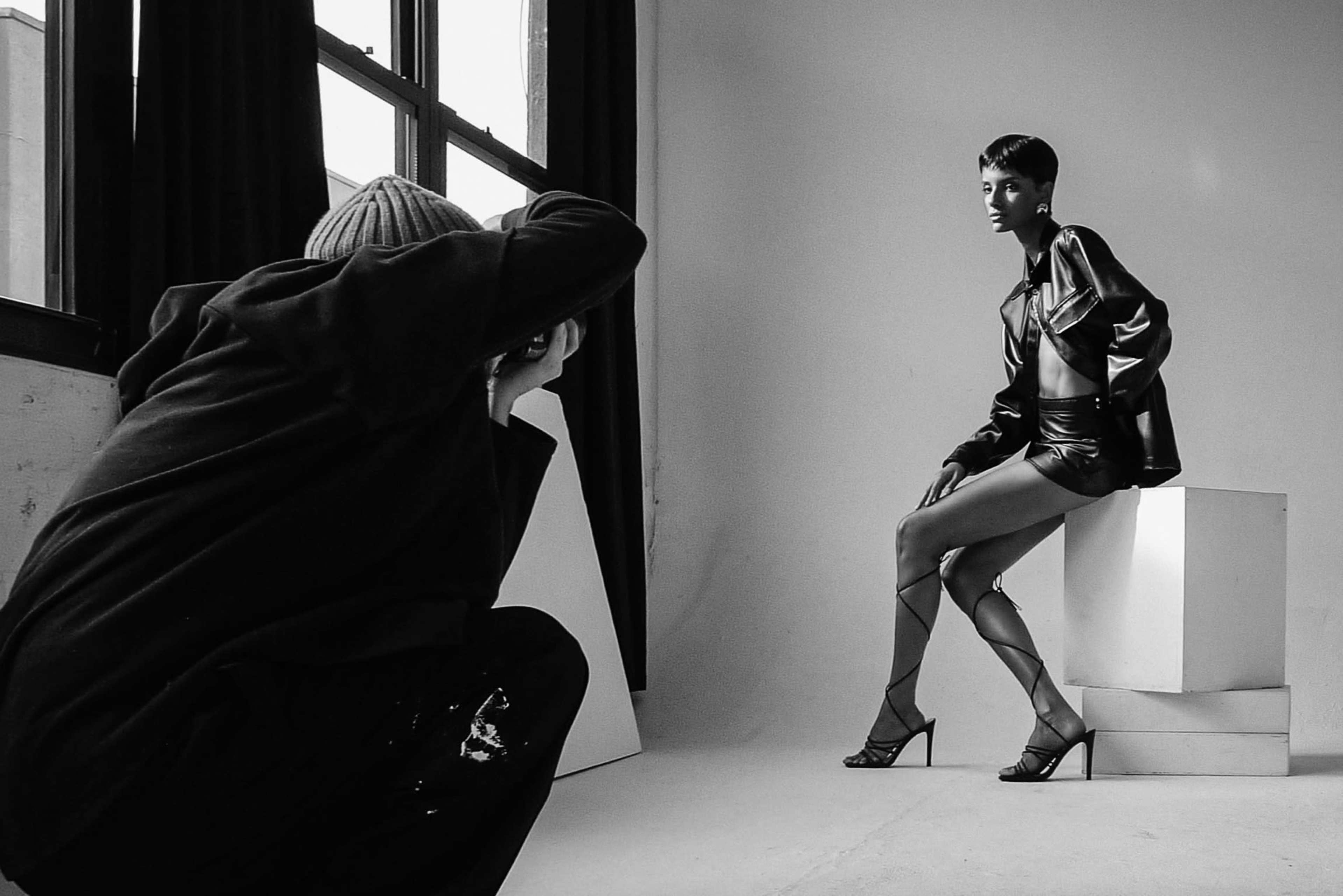 A photographer captures a model posing in high fashion attire in a studio setting.