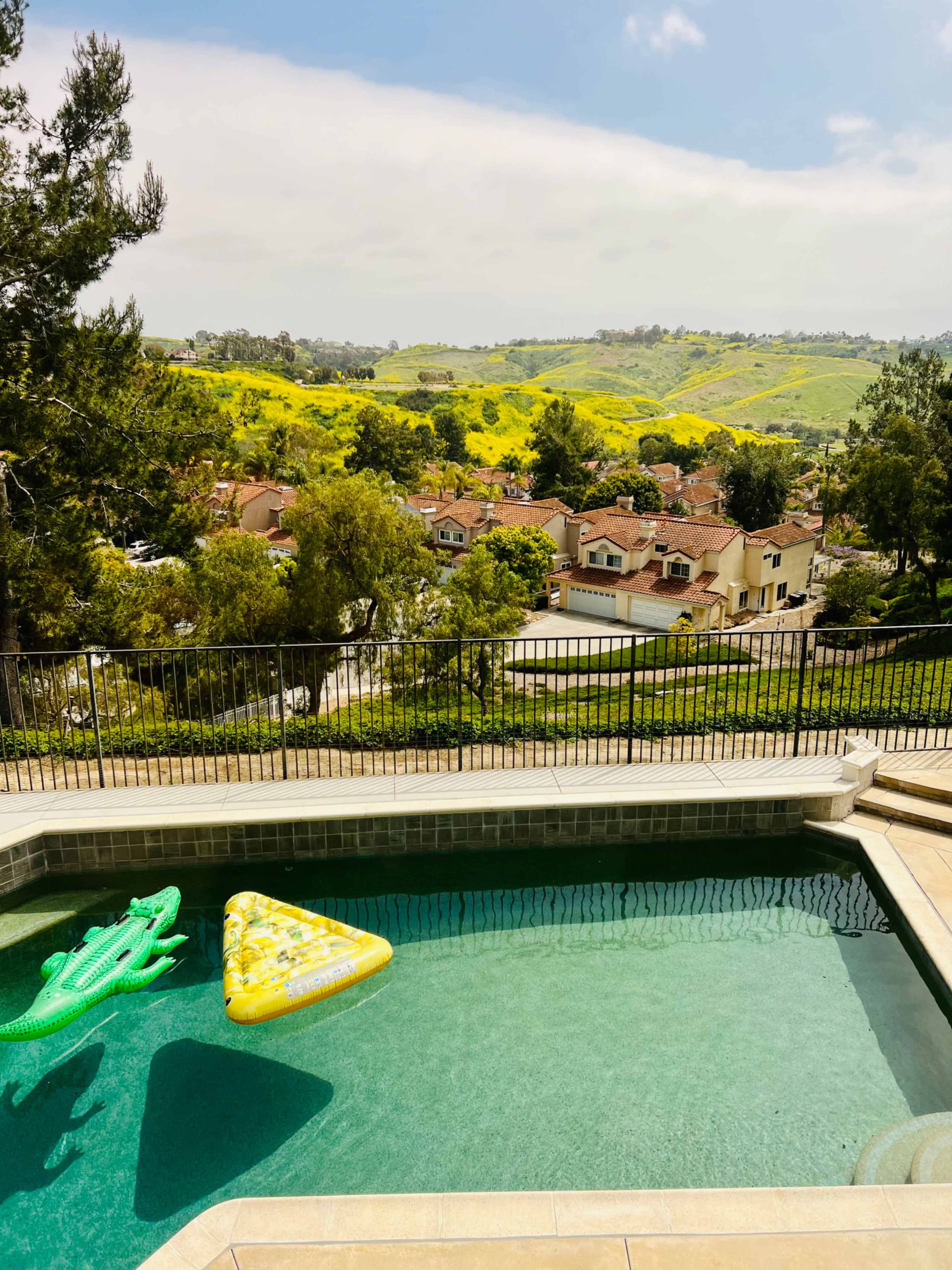 A clear swimming pool with two inflated float toys overlooks a scenic view of rolling green hills and residential homes.