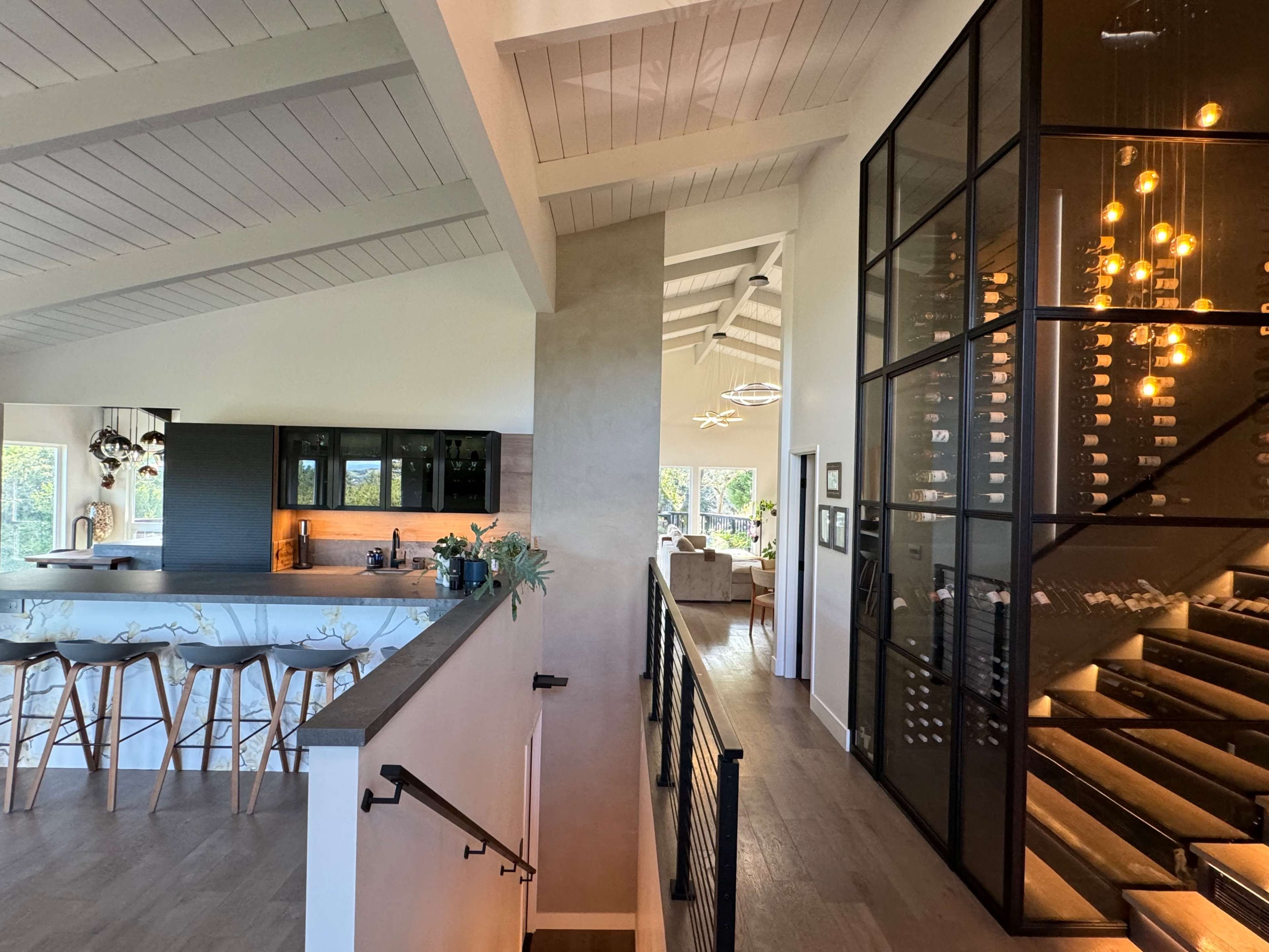 A modern interior with an open-concept kitchen and dining area on the left and a staircase enclosed in glass featuring a wine storage area on the right.