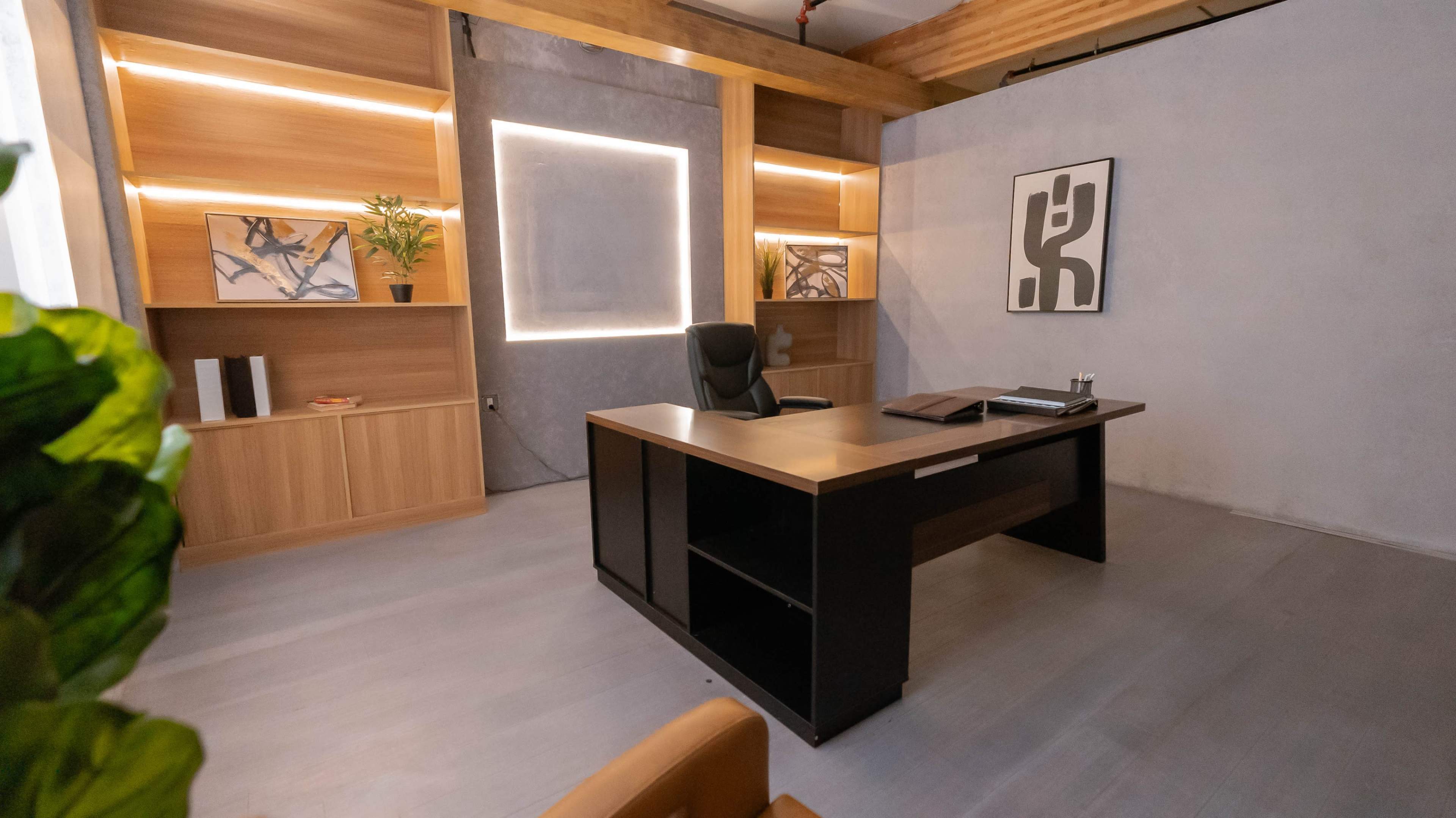 The image shows a modern office space featuring a sleek wooden desk, a black office chair, and minimalist decor on the walls.