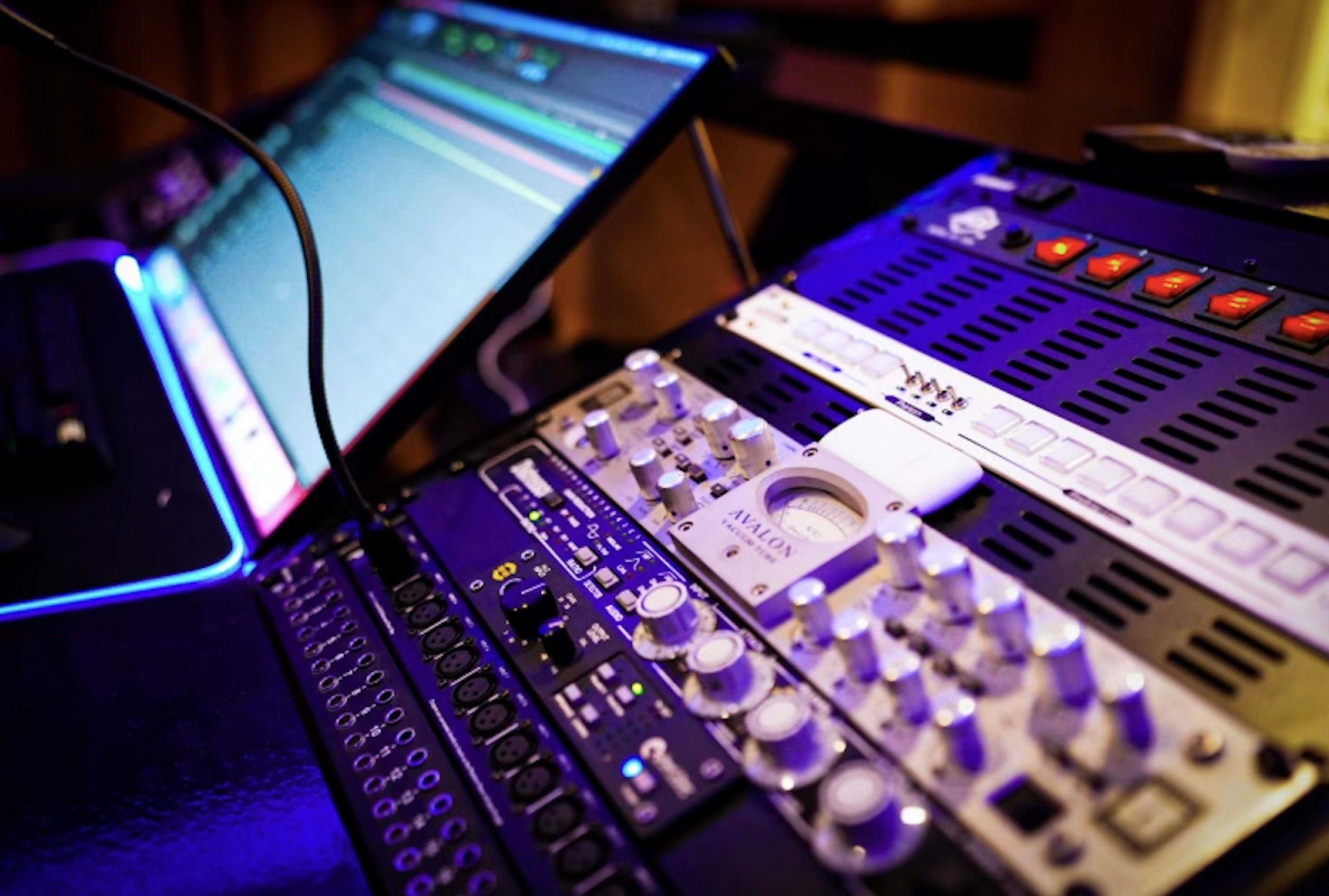 A close-up view of a digital audio workstation with a computer monitor displaying audio tracks and a mixing console featuring various knobs and sliders.