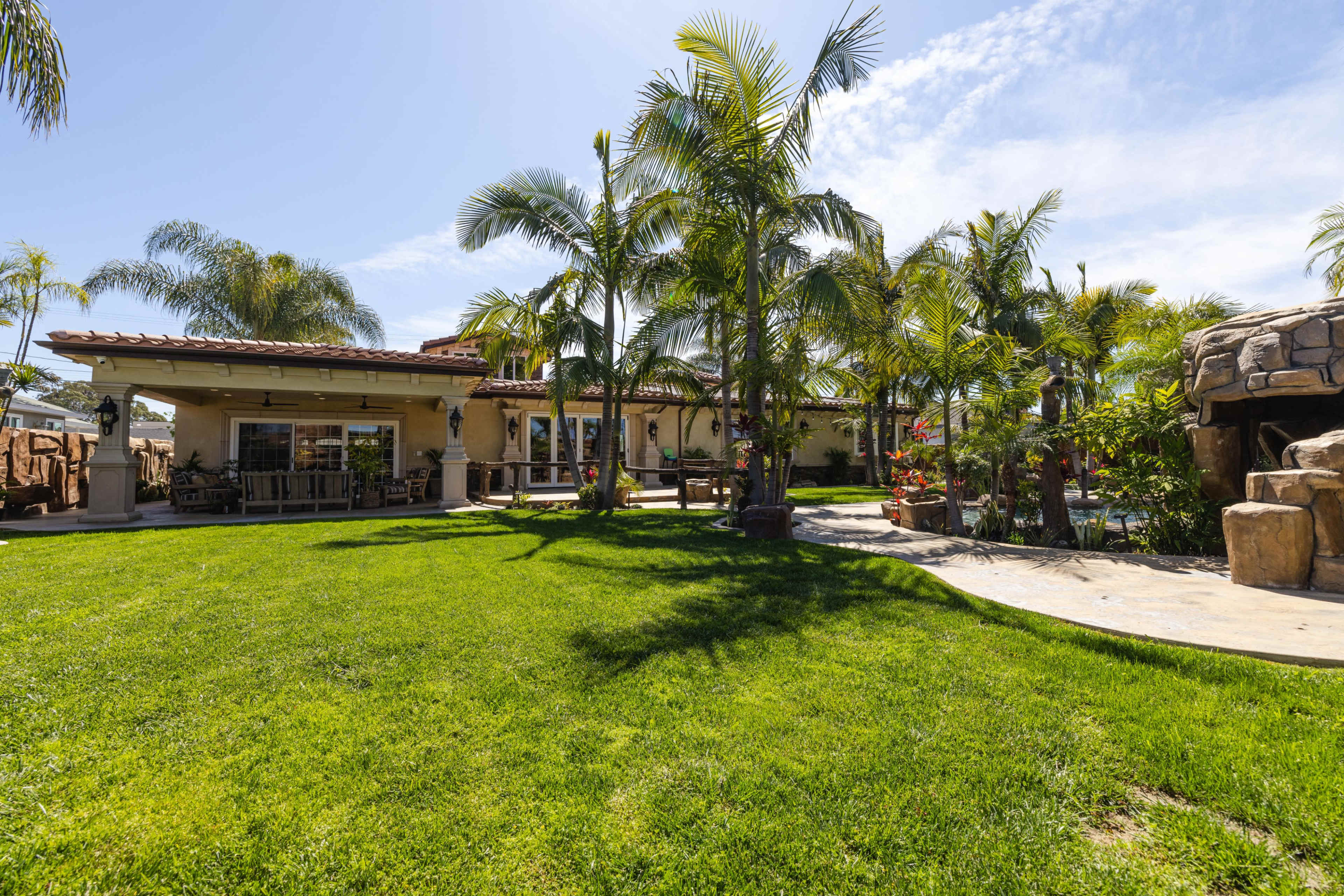 A spacious backyard with lush green grass, palm trees, and a villa-style house in the background.