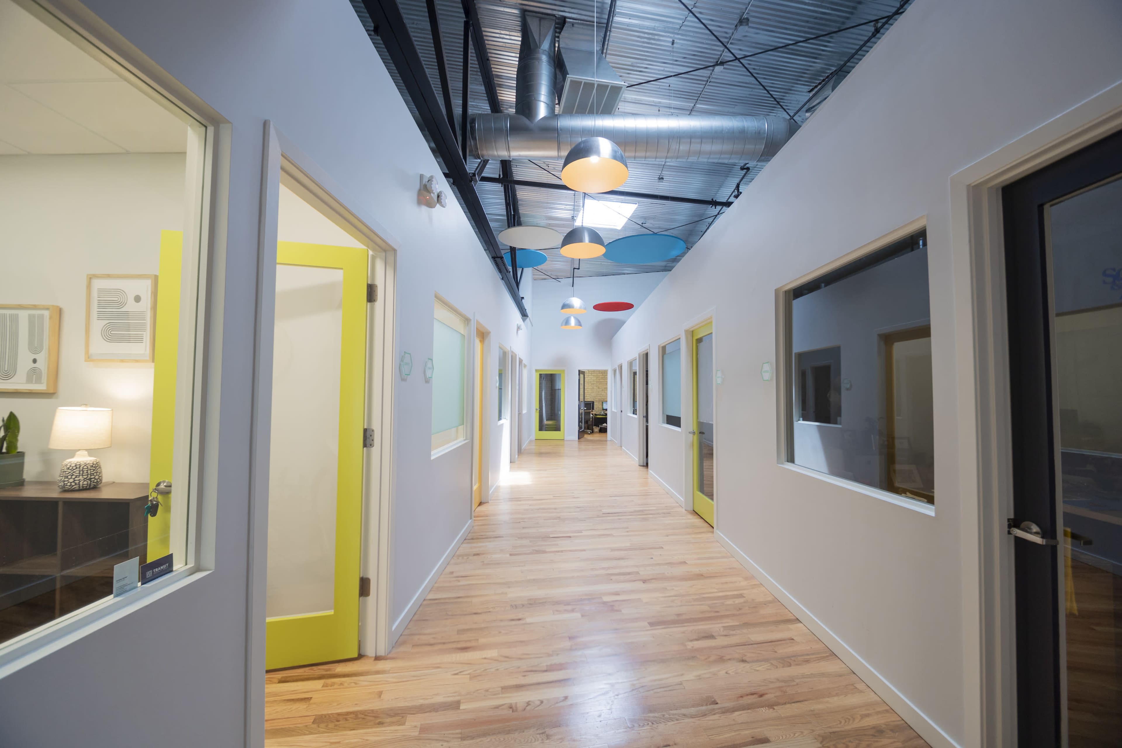 A brightly lit hallway features yellow doors along white walls with wooden flooring and colorful ceiling lights.