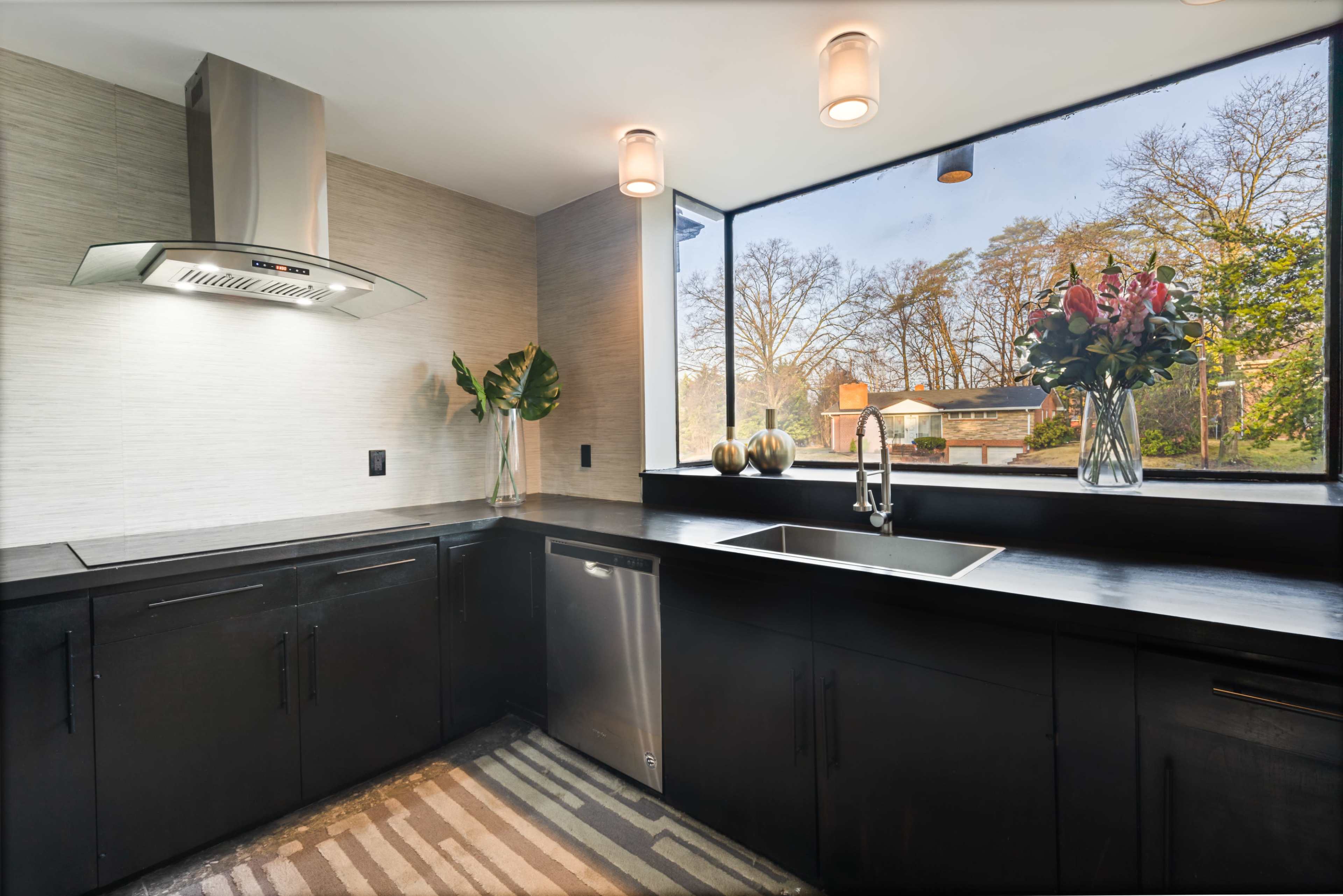 A modern kitchen features dark cabinetry, stainless steel appliances, and a large window with a view of the outdoors.