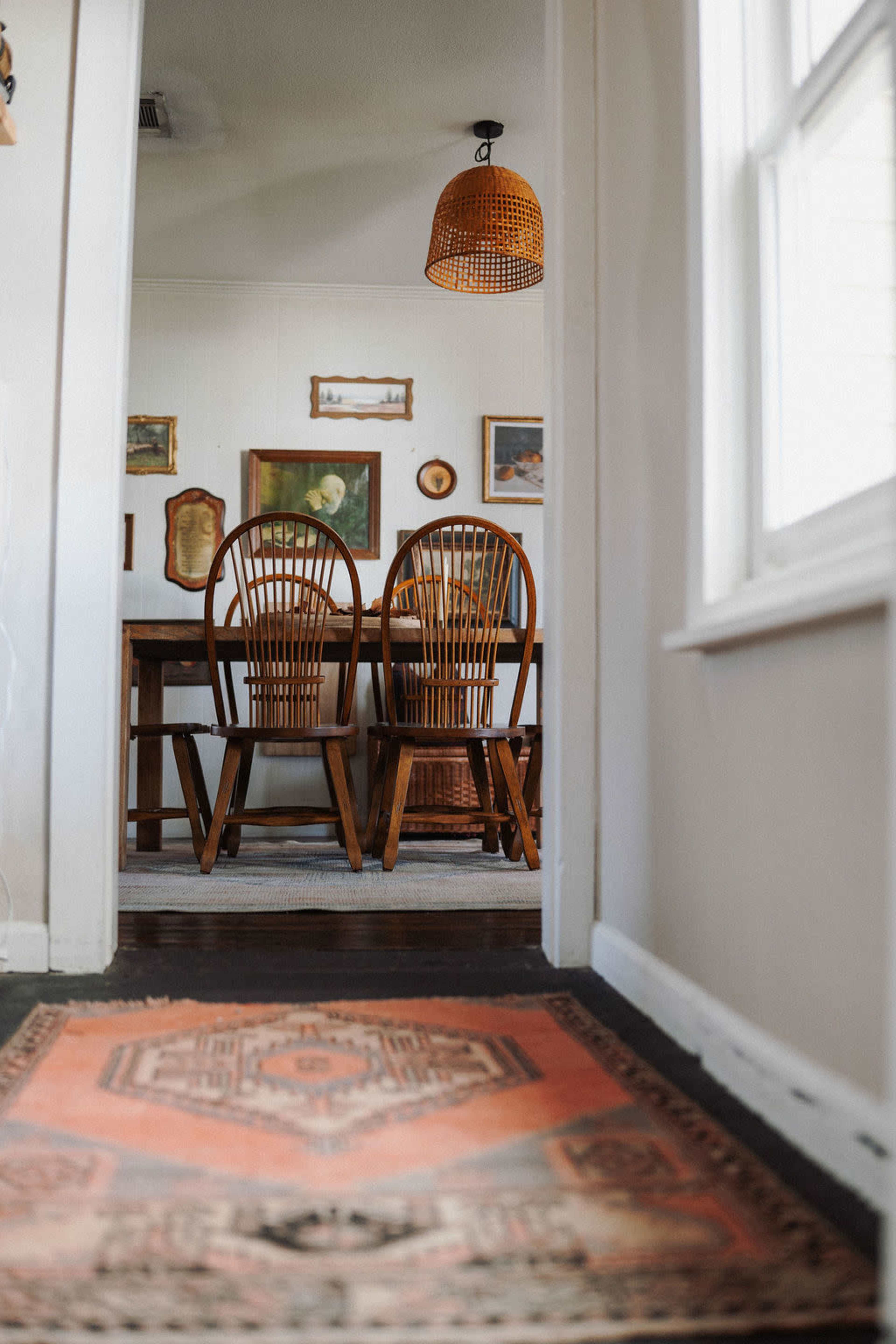 A hallway leads to a dining area featuring two wooden chairs and framed artwork on the walls.