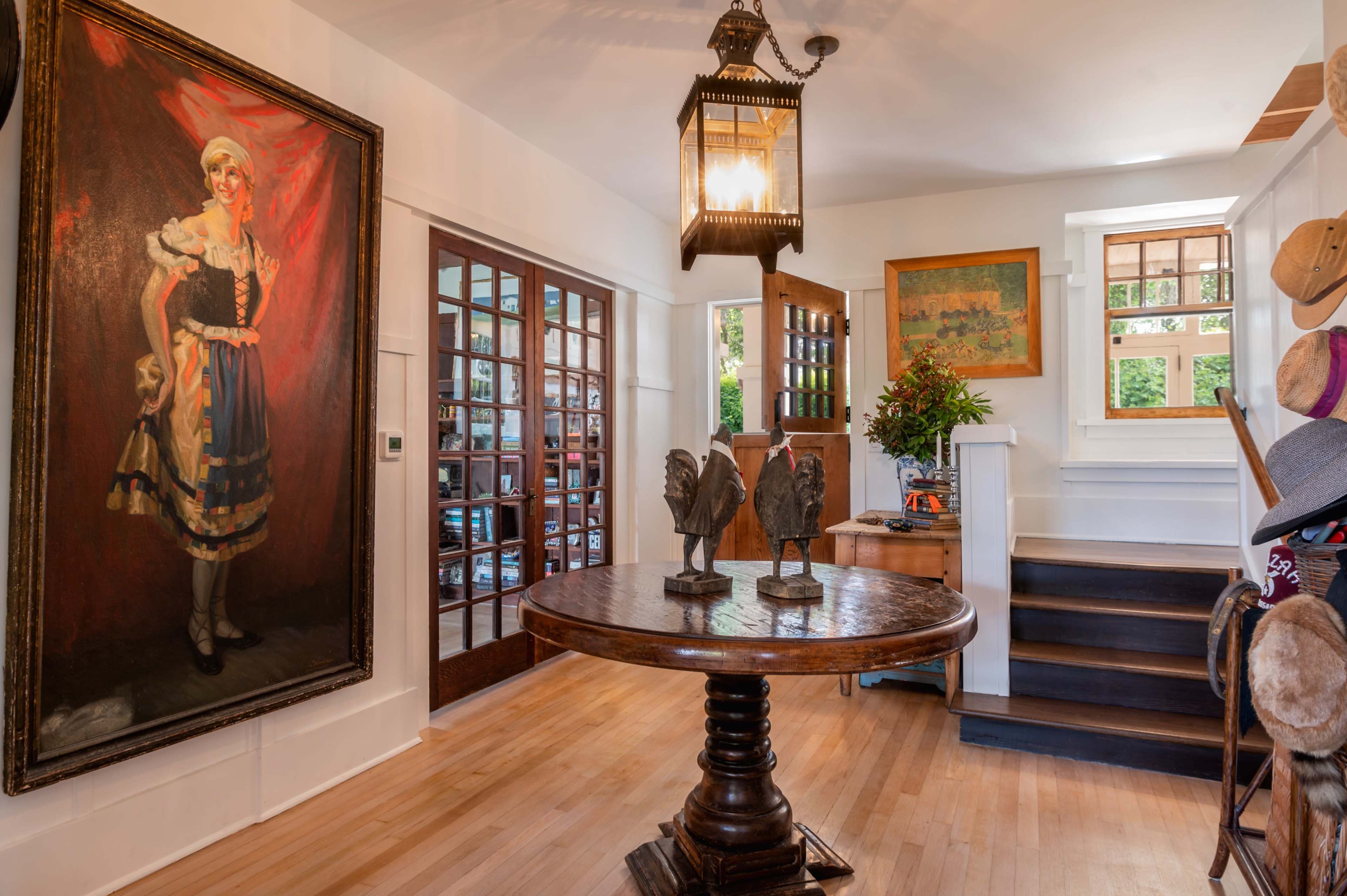 A foyer with a large painting of a woman in traditional attire, a round wooden table in the center, and a staircase leading to an upper level.