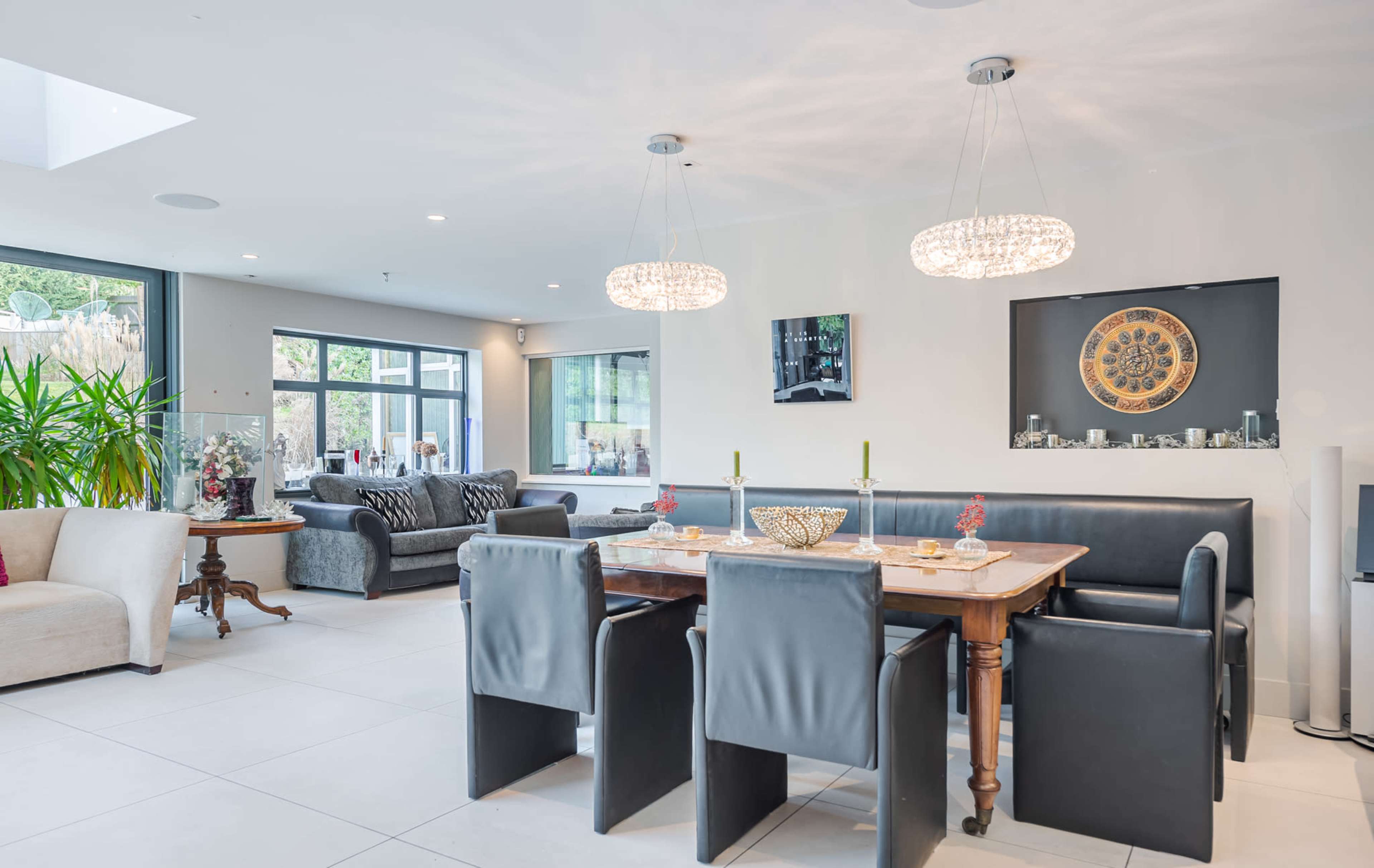 A modern dining and living area with a table set for dining, surrounded by plush seating and large windows allowing natural light.