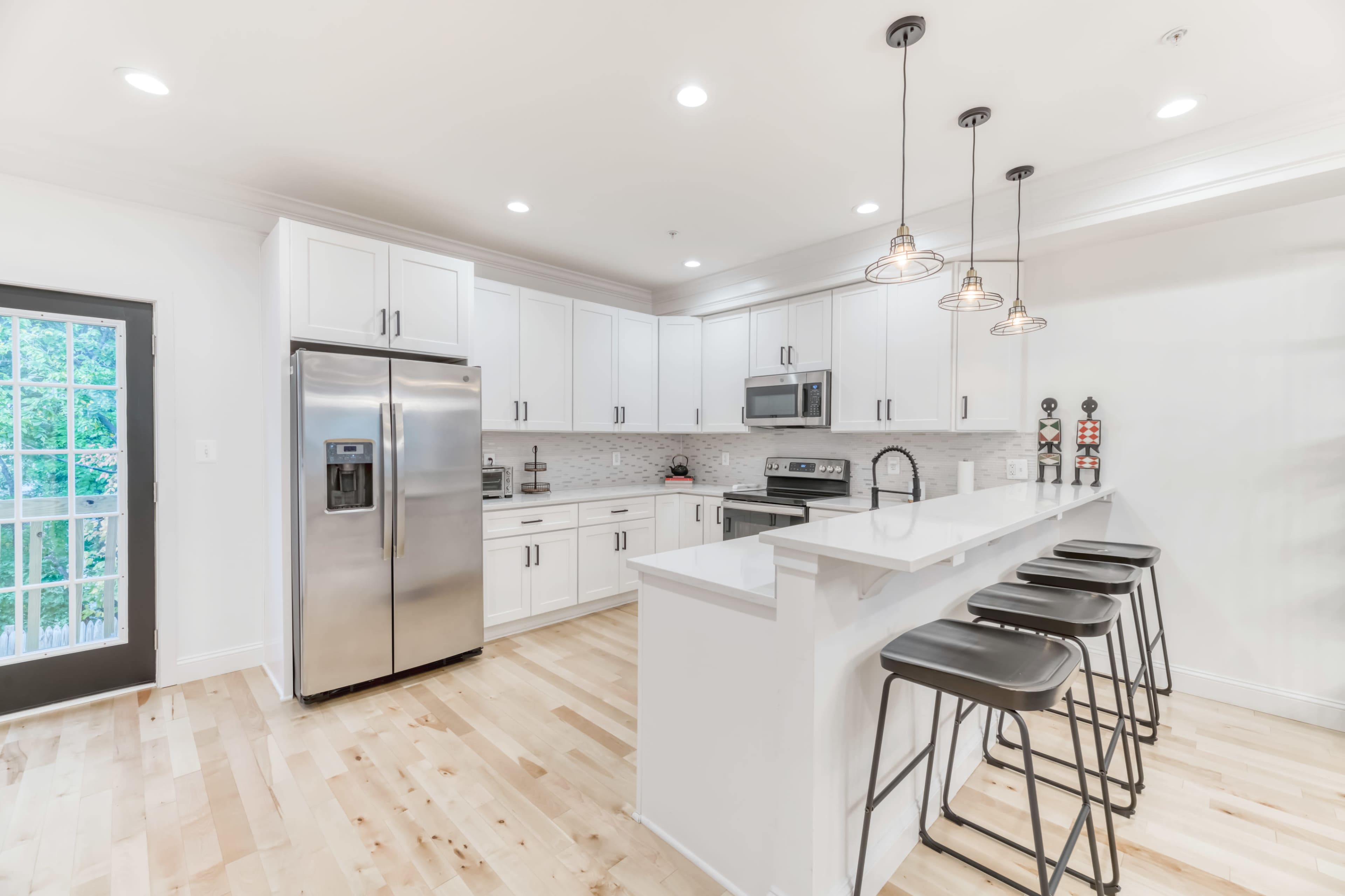 The kitchen features white cabinetry, stainless steel appliances, and a bar with four black stools.