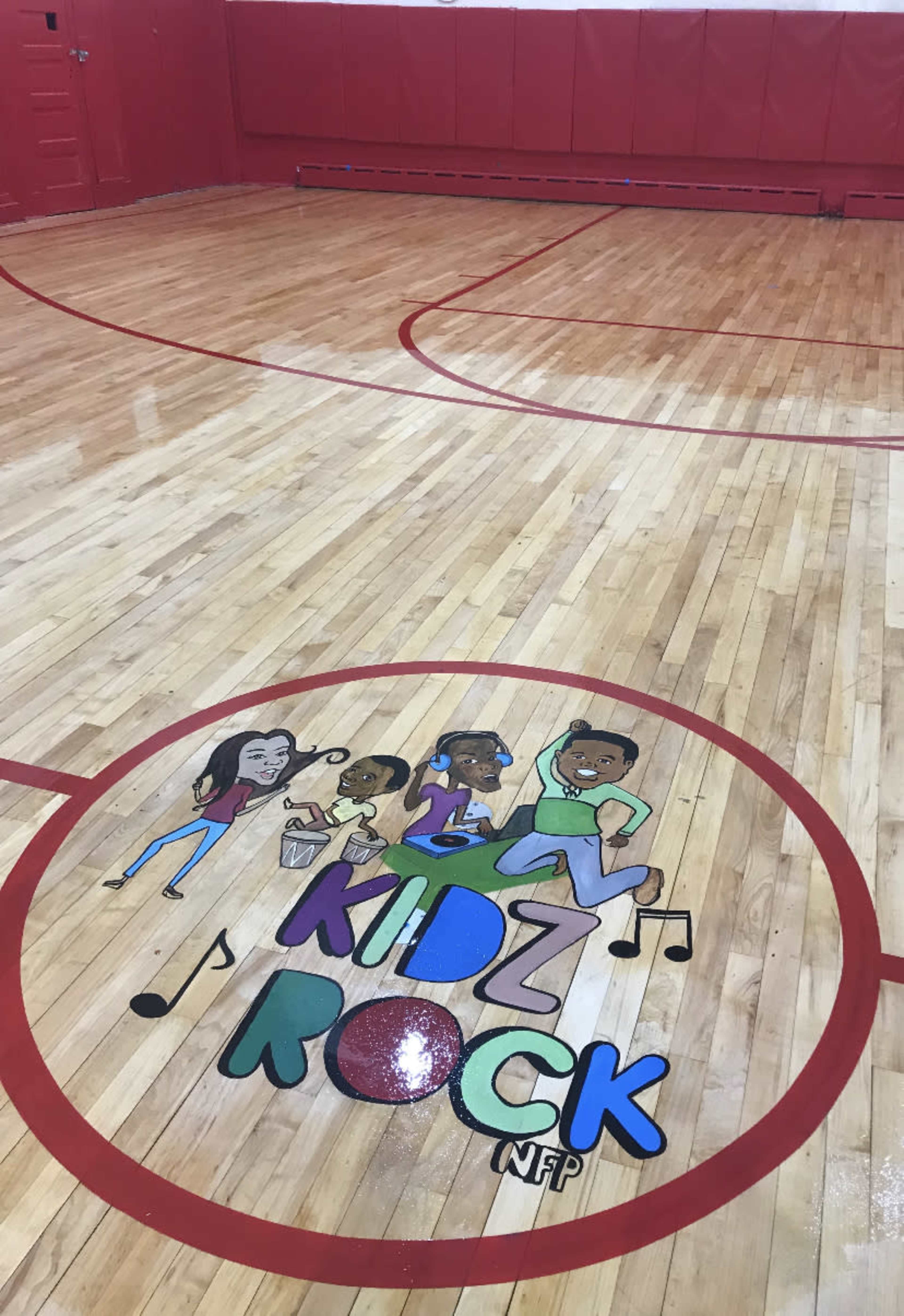 The wooden gym floor features a painted logo in the center that reads "KIDZ ROCK" with cartoon figures and musical notes.