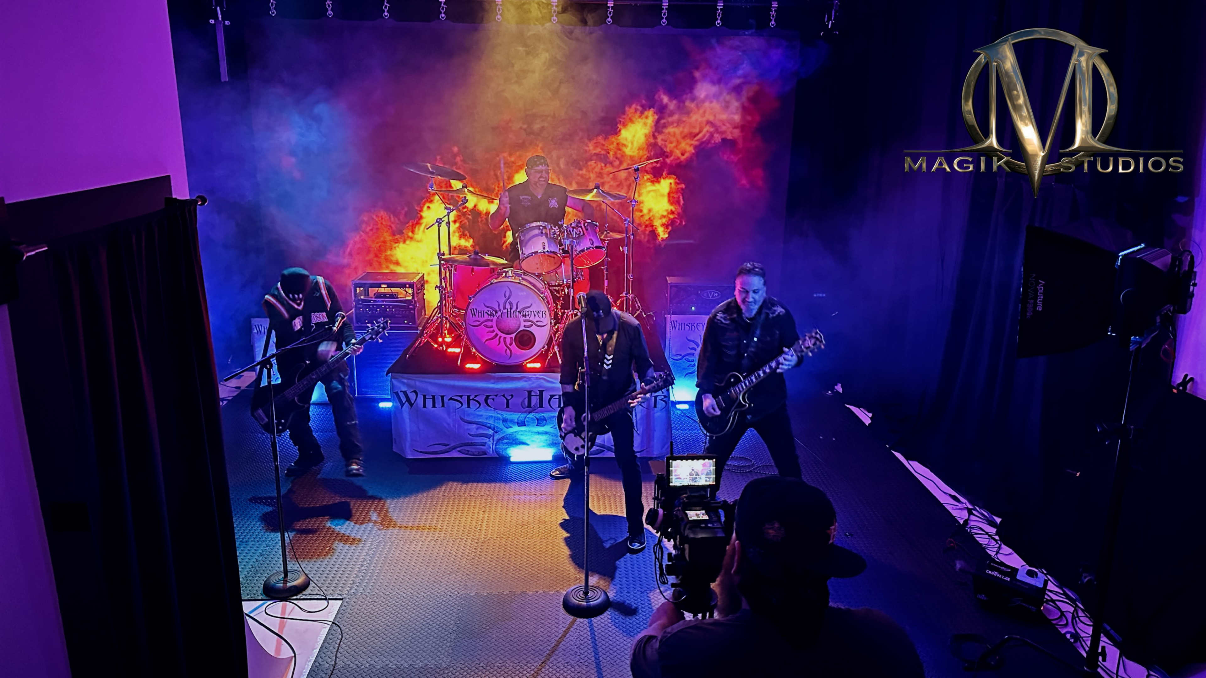 A rock band performs on stage with colorful smoke effects and a drummer in the background.