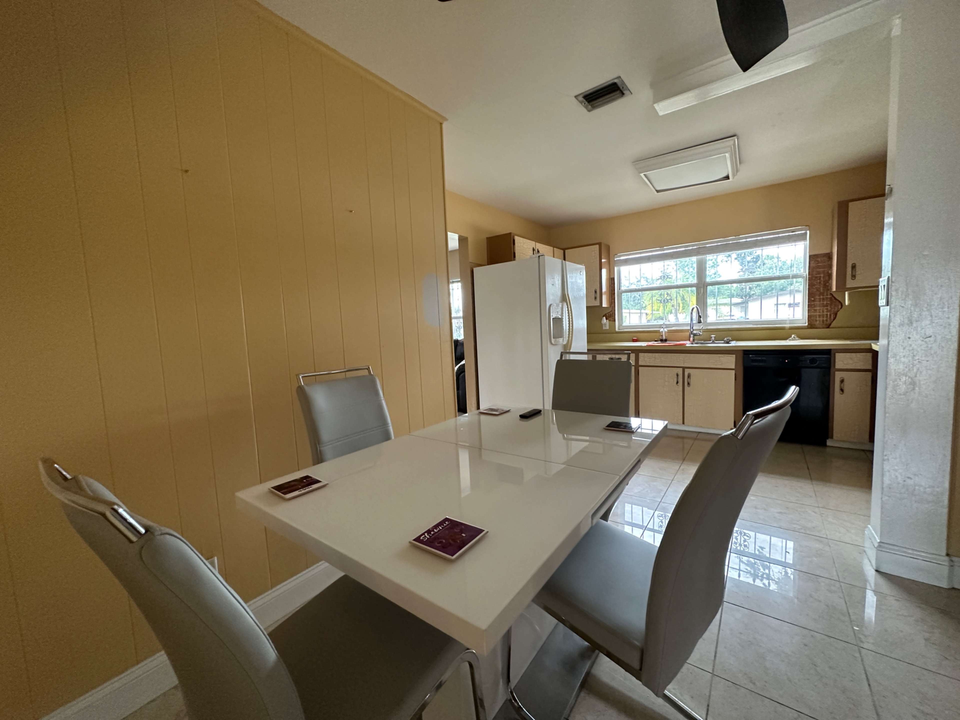 A modern kitchen features a light-colored table surrounded by four chairs, with appliances and cabinets visible in the background.