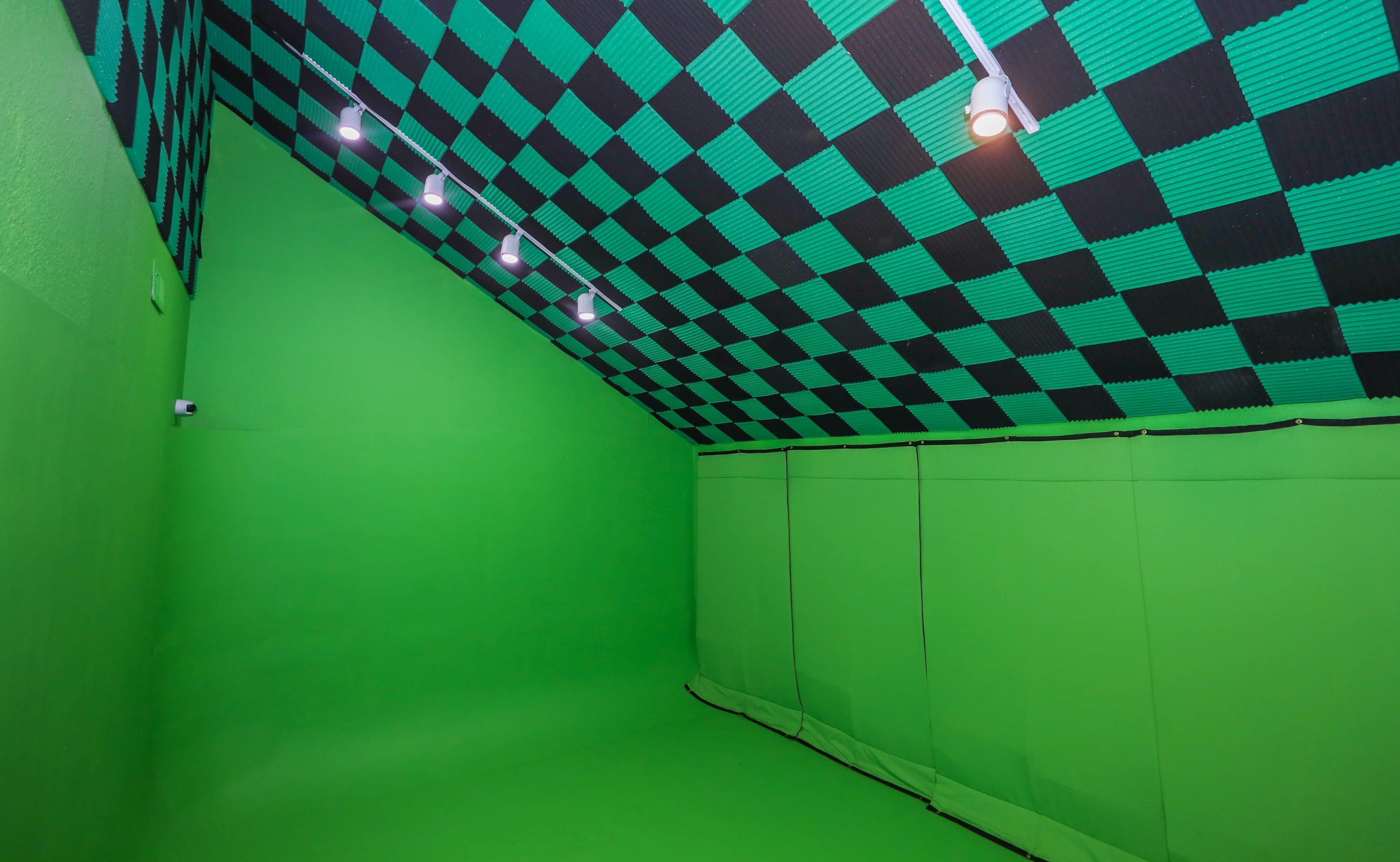 The room features a green backdrop with a black and green checkered ceiling and is equipped with four spotlights.