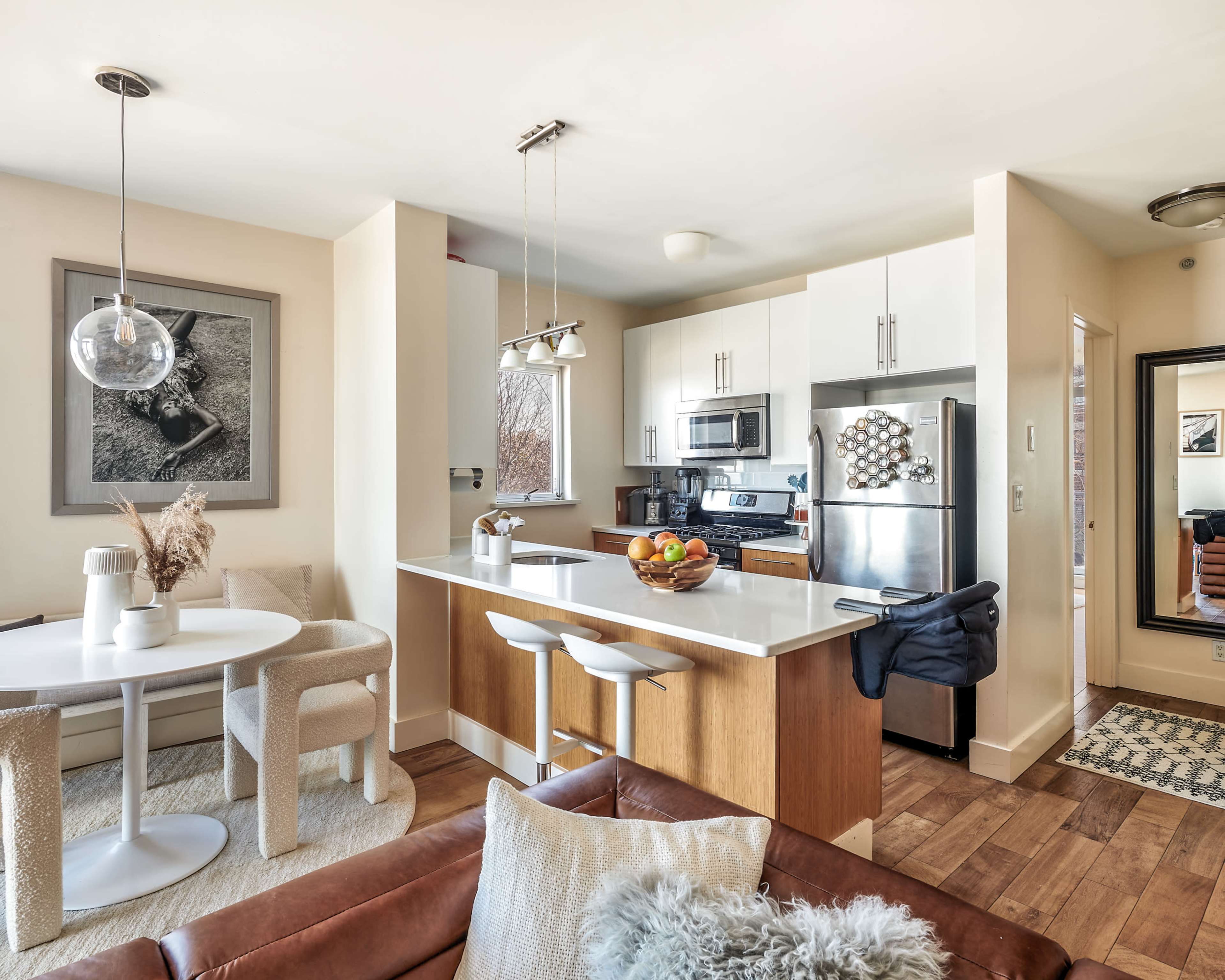 A modern kitchen and dining area feature a circular table with chairs, a sleek white island, and stainless steel appliances.