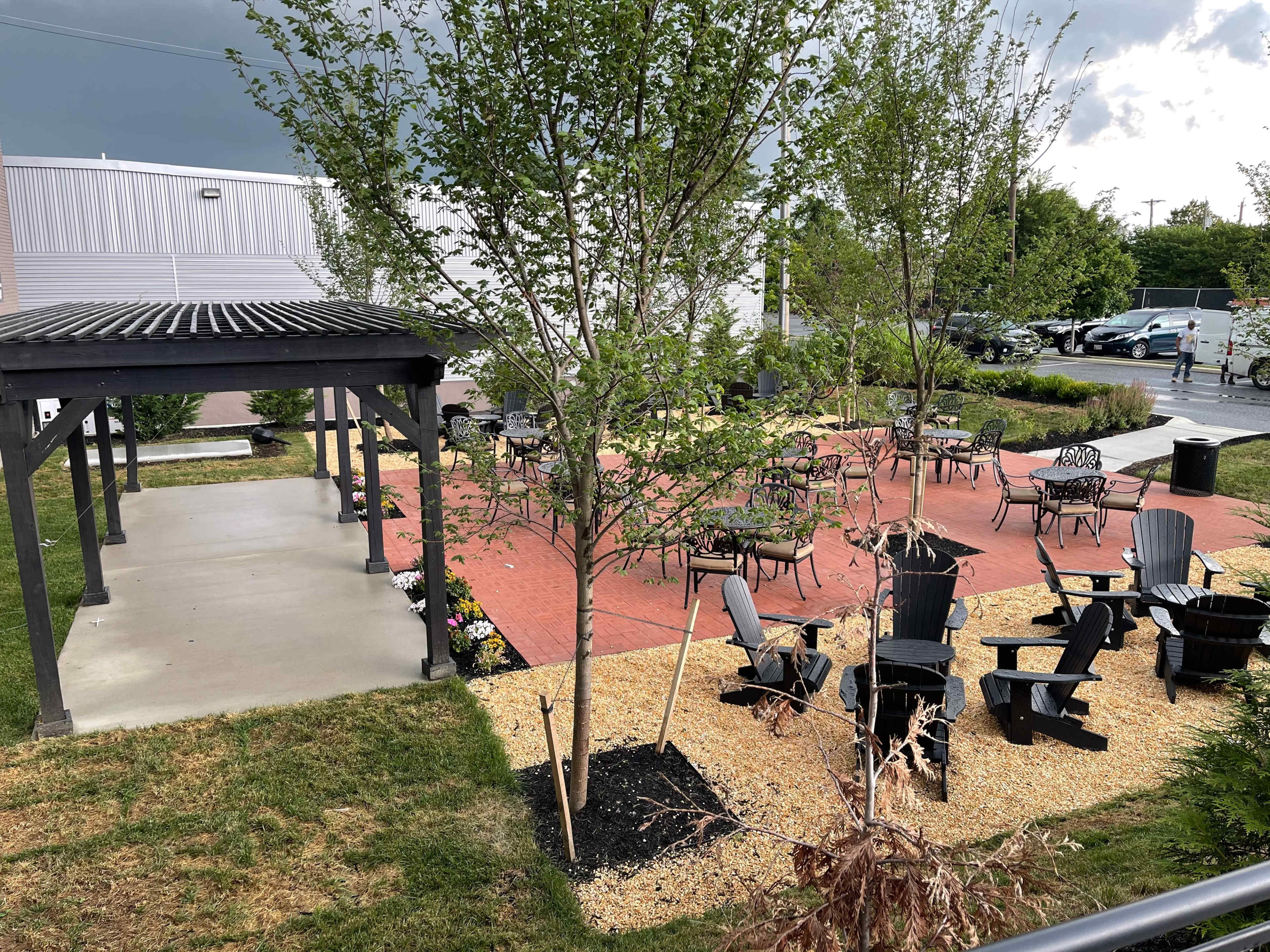 A landscaped outdoor patio area with seating arrangements, including black chairs and tables, surrounded by gravel and trees.