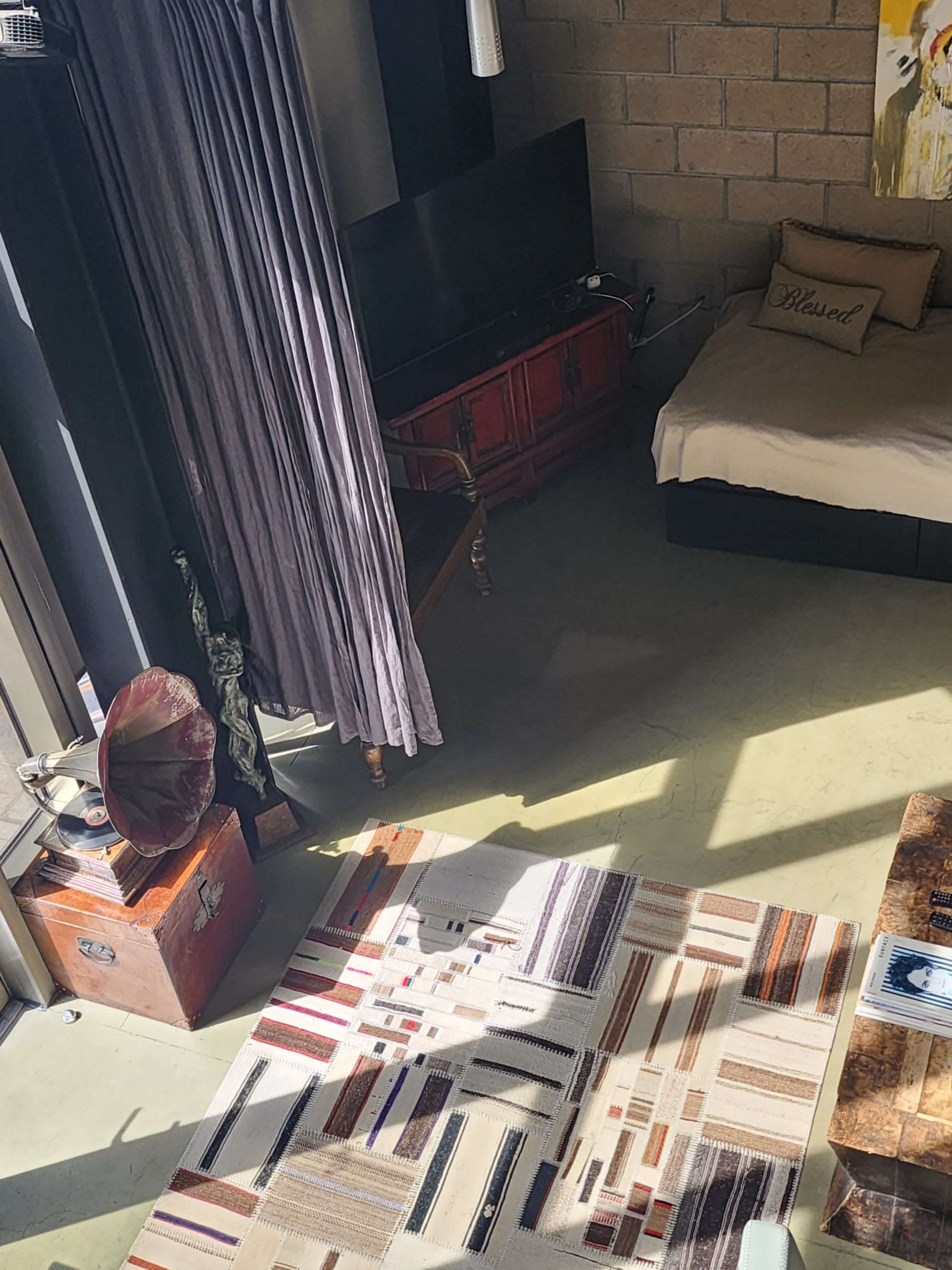 A cozy bedroom with a bed, a vintage-style television stand, a gramophone, and a patterned area rug on a polished floor.