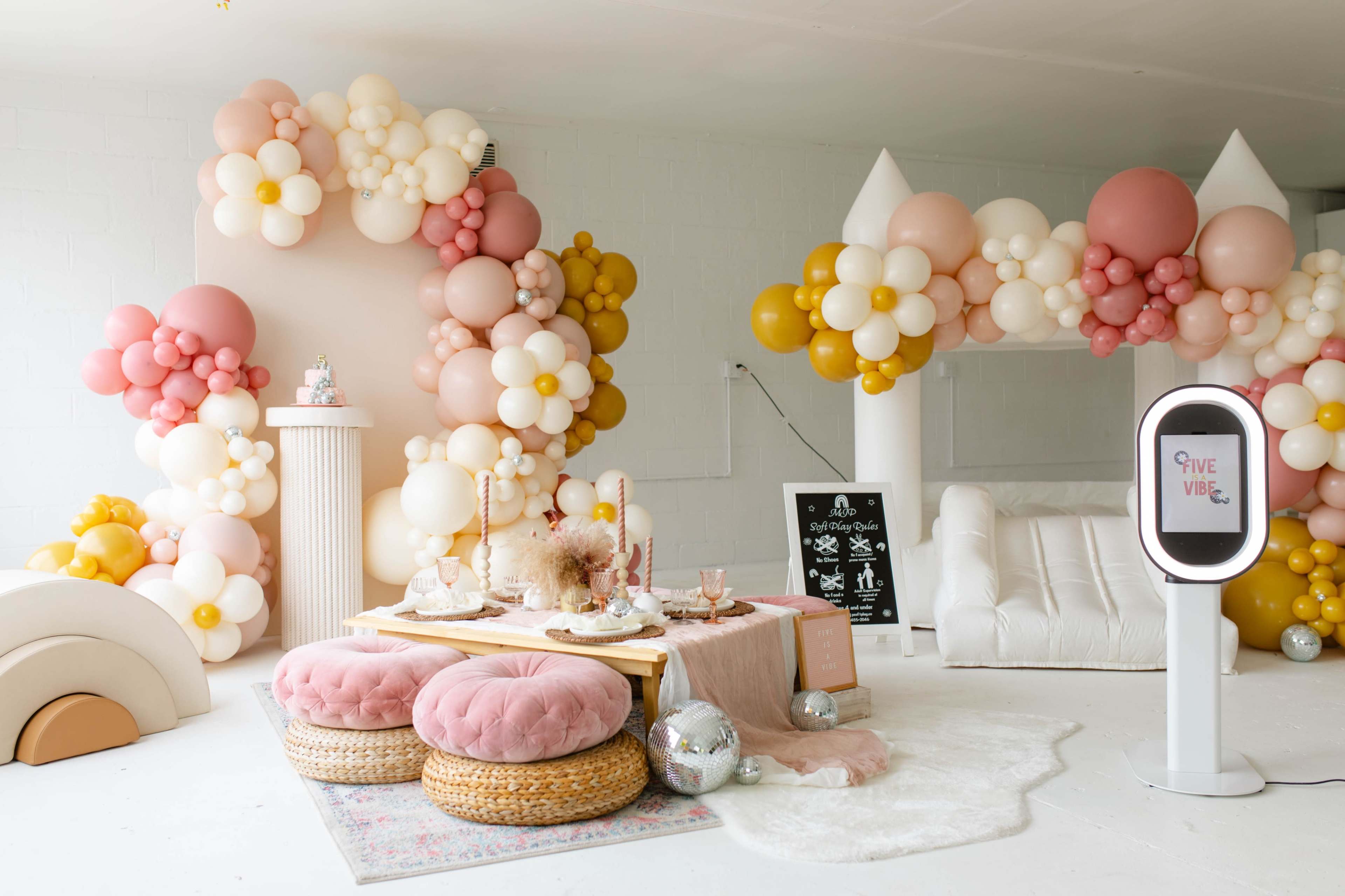 A decorated event space with balloon arches, a small seating area, a table adorned with snacks, and a photo booth.