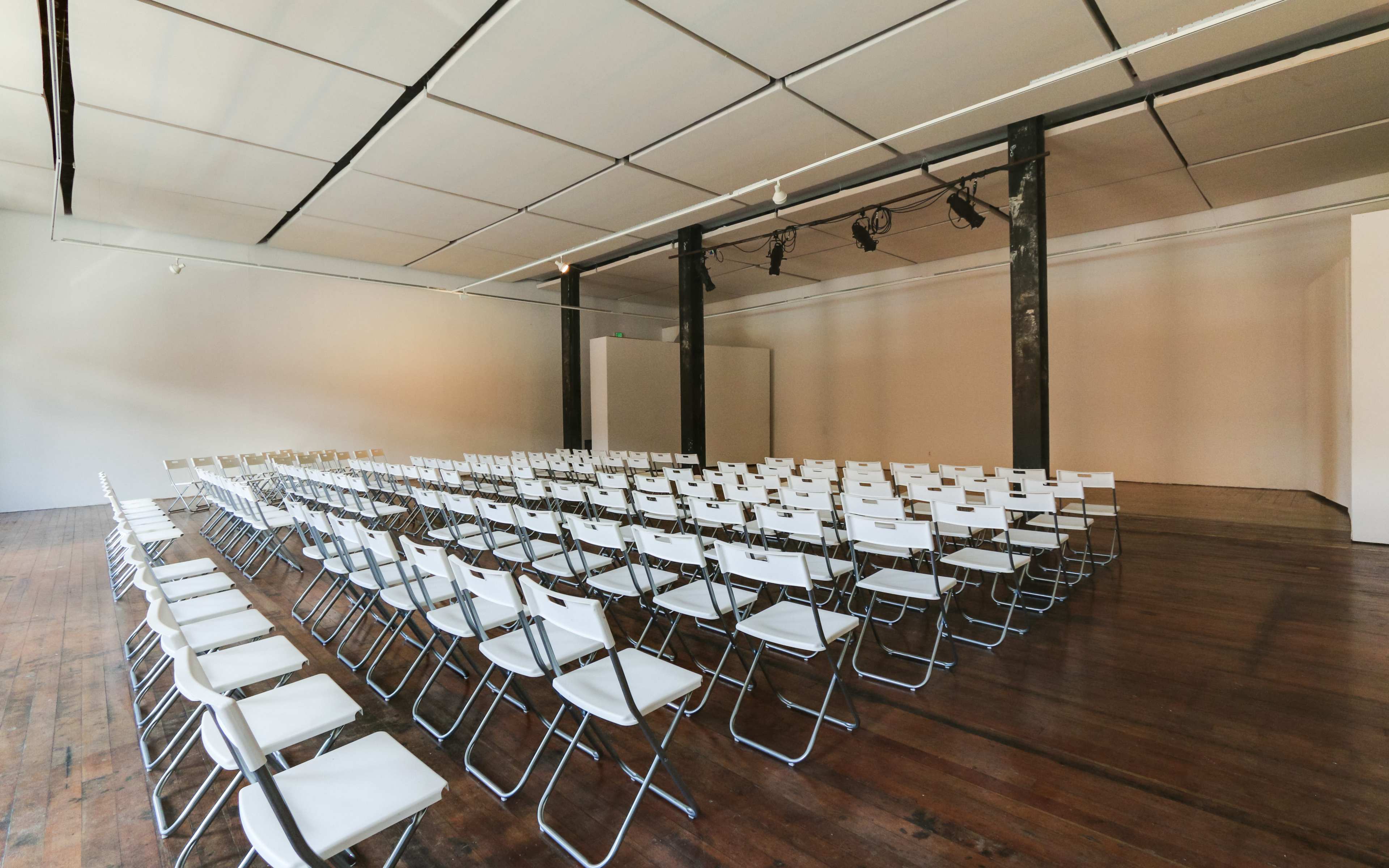 A large indoor space features several rows of white folding chairs arranged facing a blank wall.