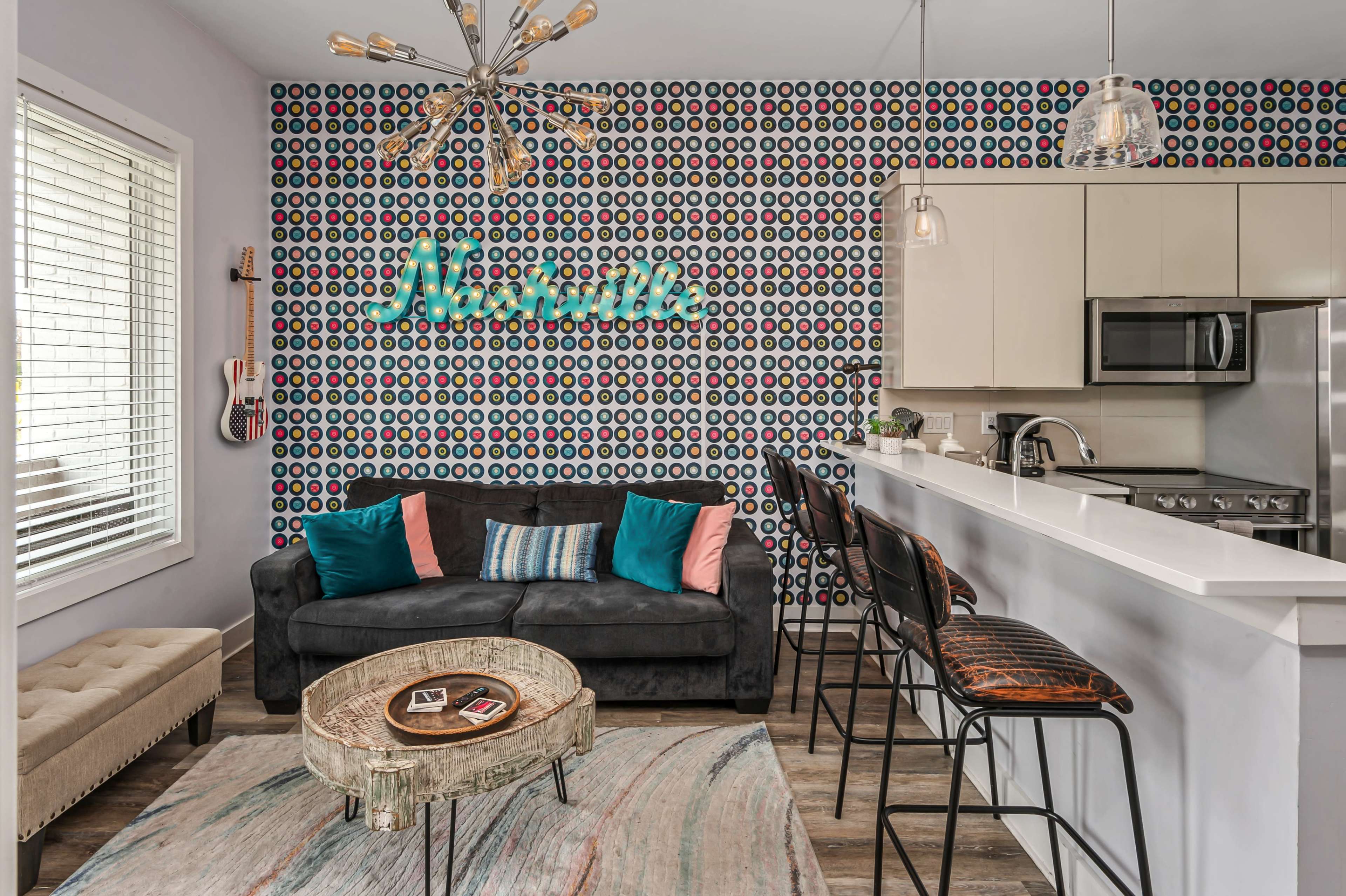 A modern living space with a patterned accent wall, a dark sofa, a round coffee table, and a bar area with high stools.