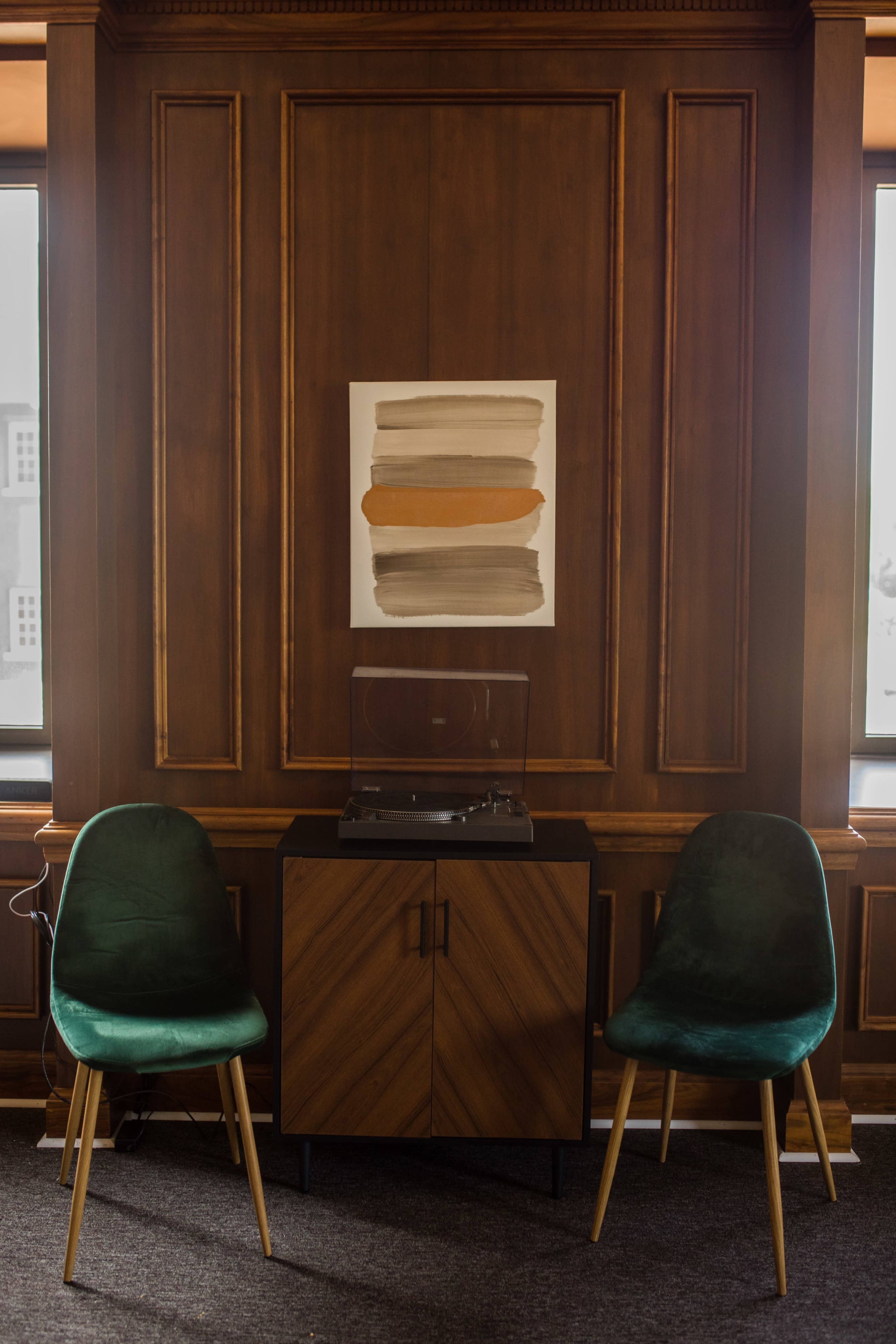A wooden-paneled room with a record player on a black cabinet between two green chairs.