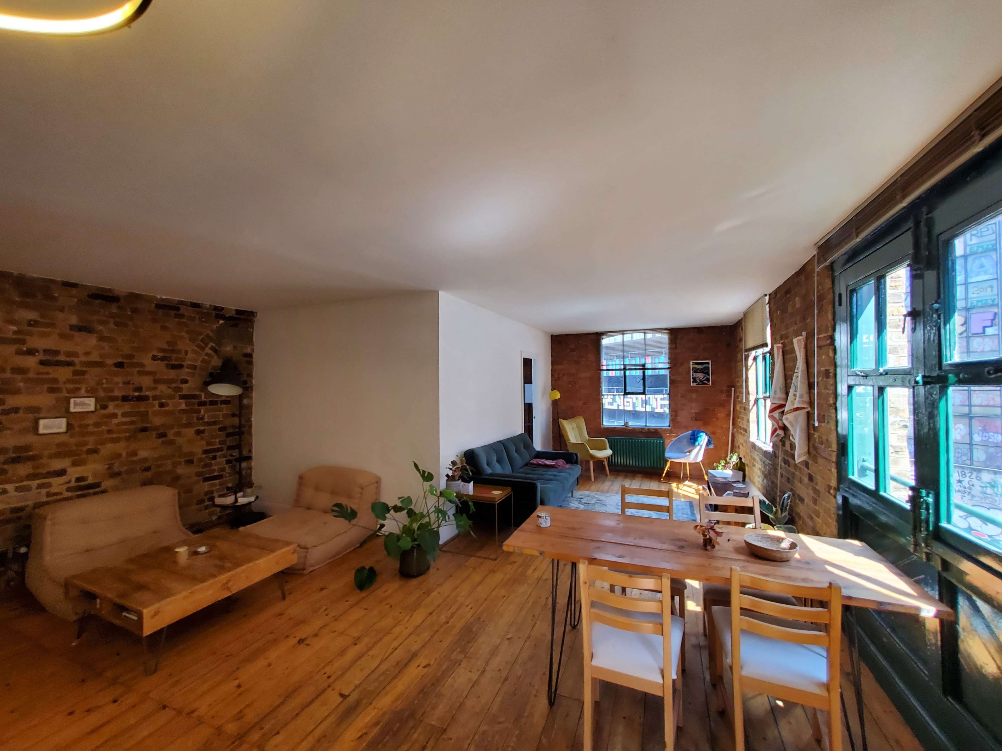 A spacious living area with exposed brick walls, wooden flooring, a dining table, and various seating arrangements.
