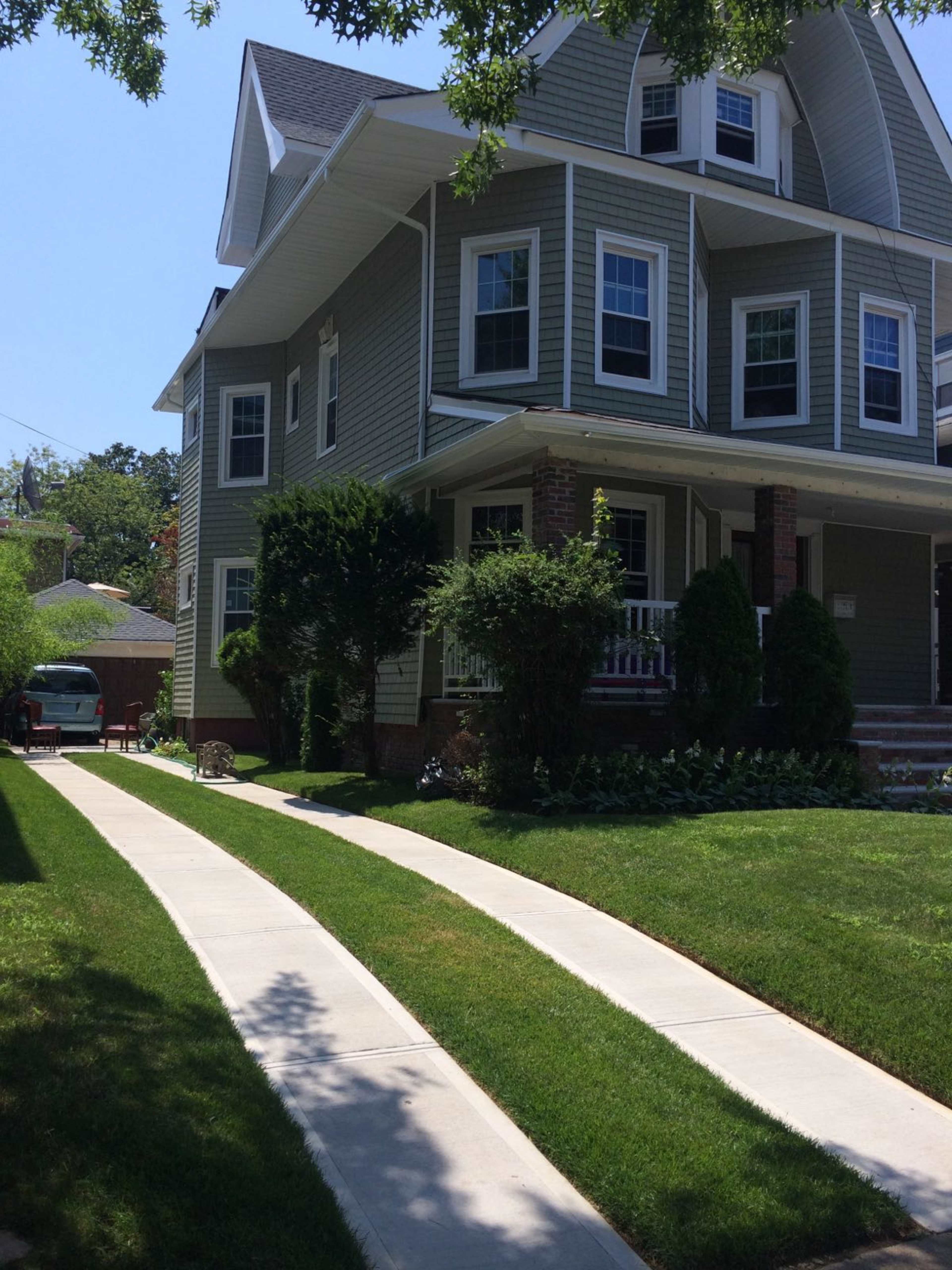 The image shows a multi-story green house with a well-maintained lawn and concrete walkways leading to the entrance.
