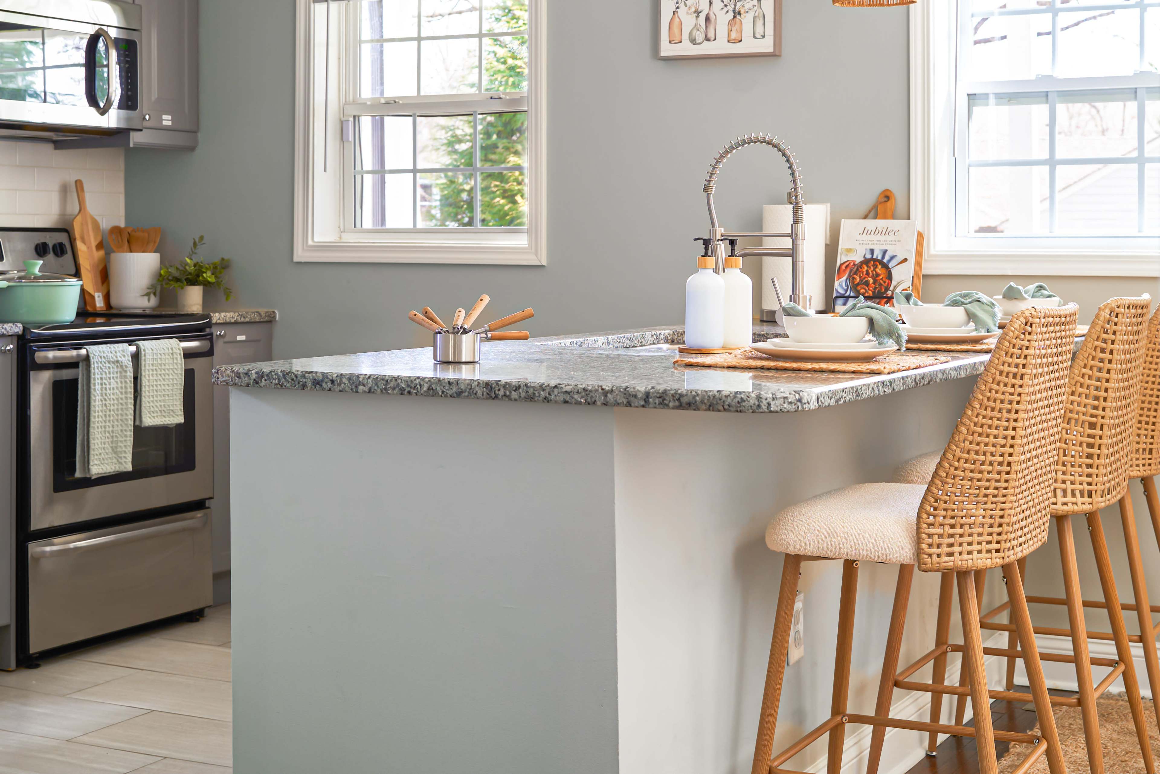 The image depicts a modern kitchen featuring a gray accent wall, a granite countertop, and three bar stools arranged around a kitchen island.