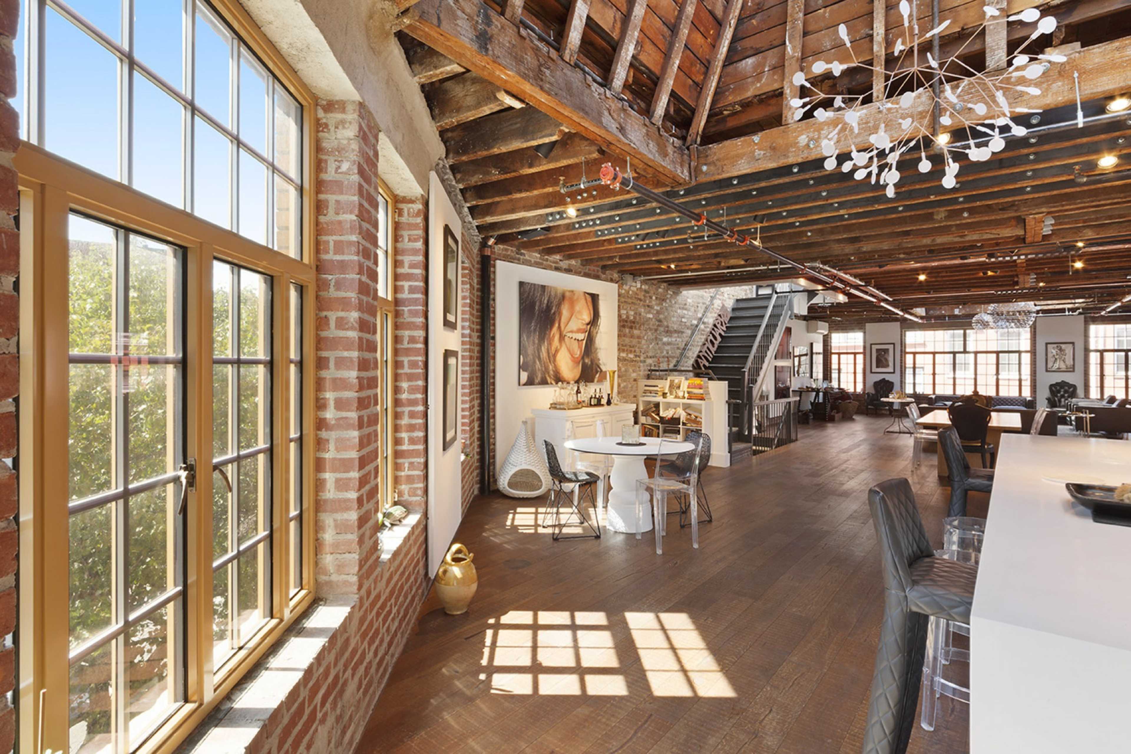 A spacious loft interior with exposed wooden beams, large windows, and a mix of modern furniture and artwork.