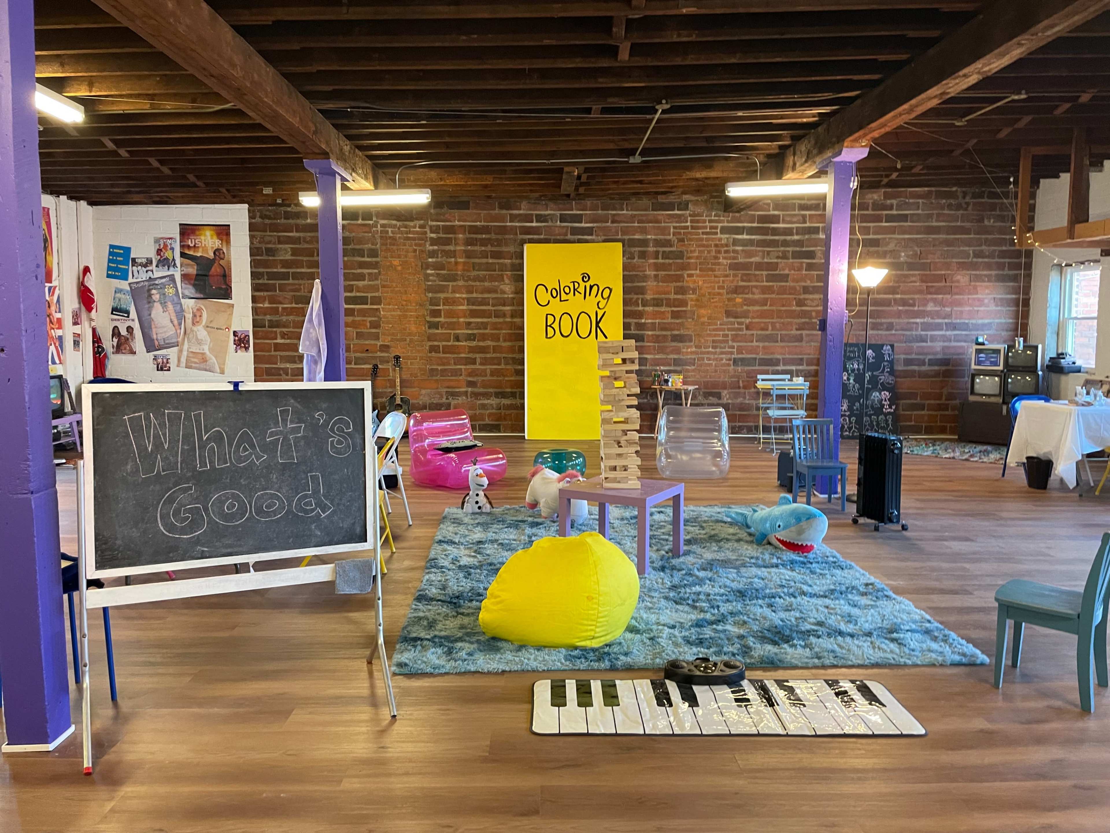 The scene shows a spacious, colorful room featuring a chalkboard, various seating options, and a large yellow display labeled "Coloring Book."