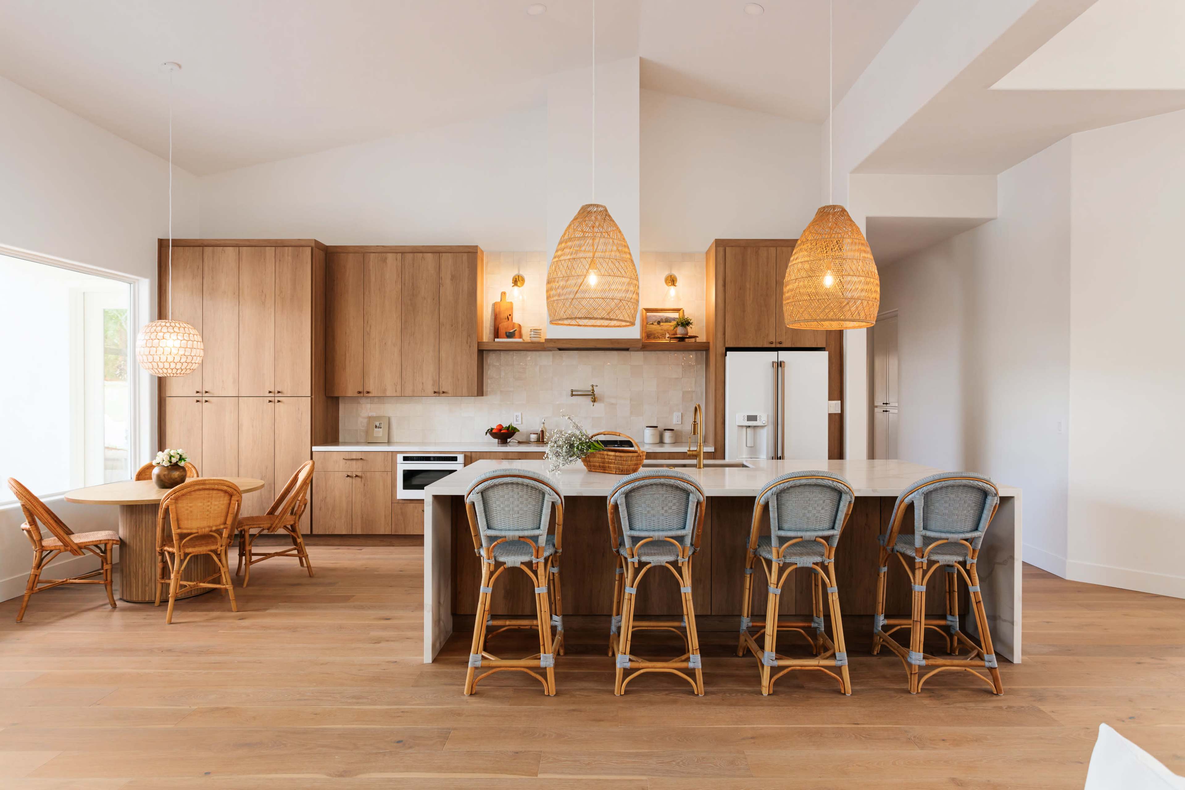 The image shows a modern kitchen with wooden cabinets, a central island with bar stools, and pendant lighting above.