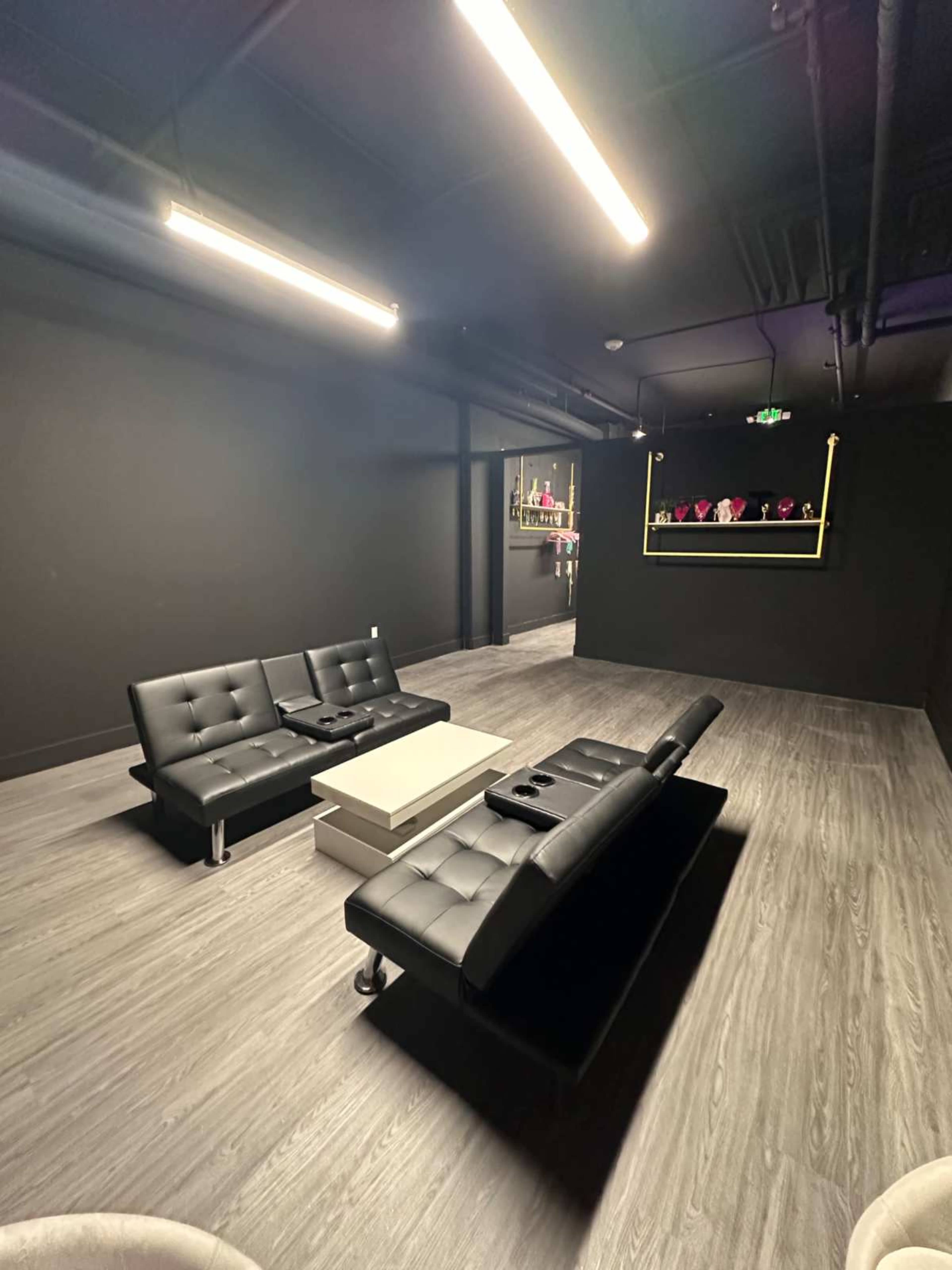 The image shows a modern lounge area with black walls, a black sectional sofa, and a low coffee table in the center.