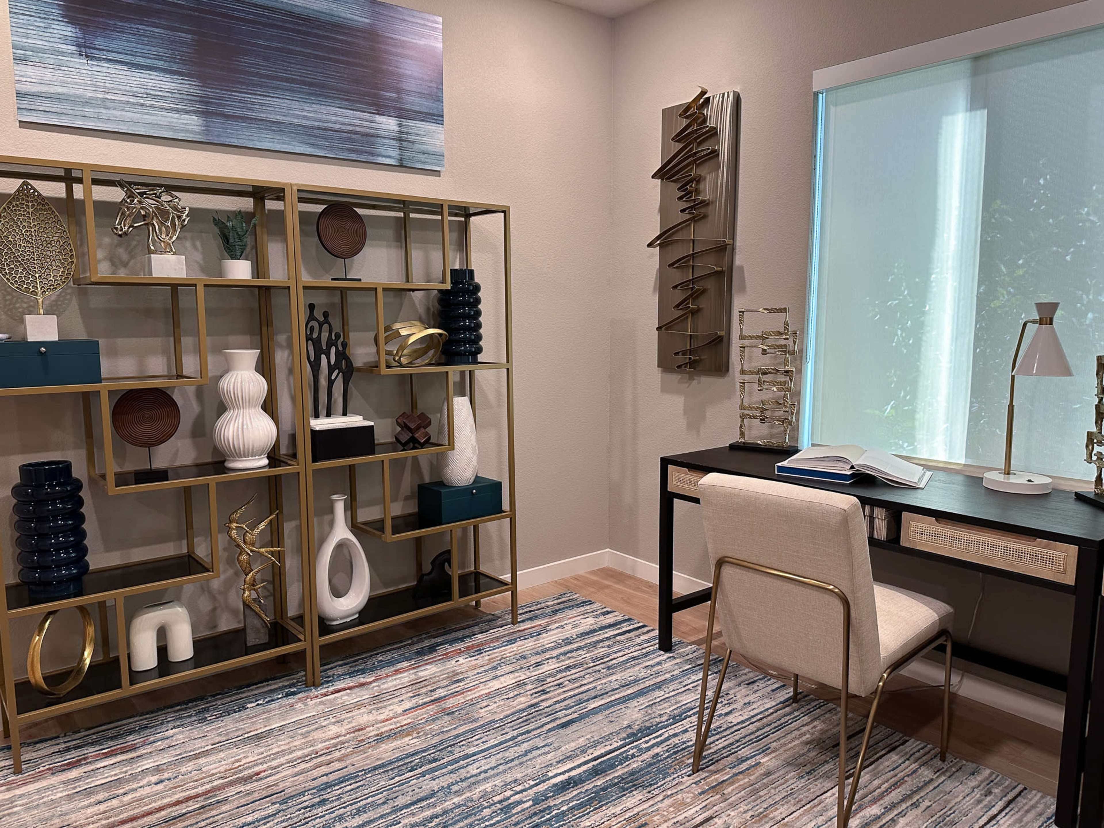 The image shows a modern home office with a desk, a chair, and a decorative shelving unit filled with various ornaments against a light-colored wall.