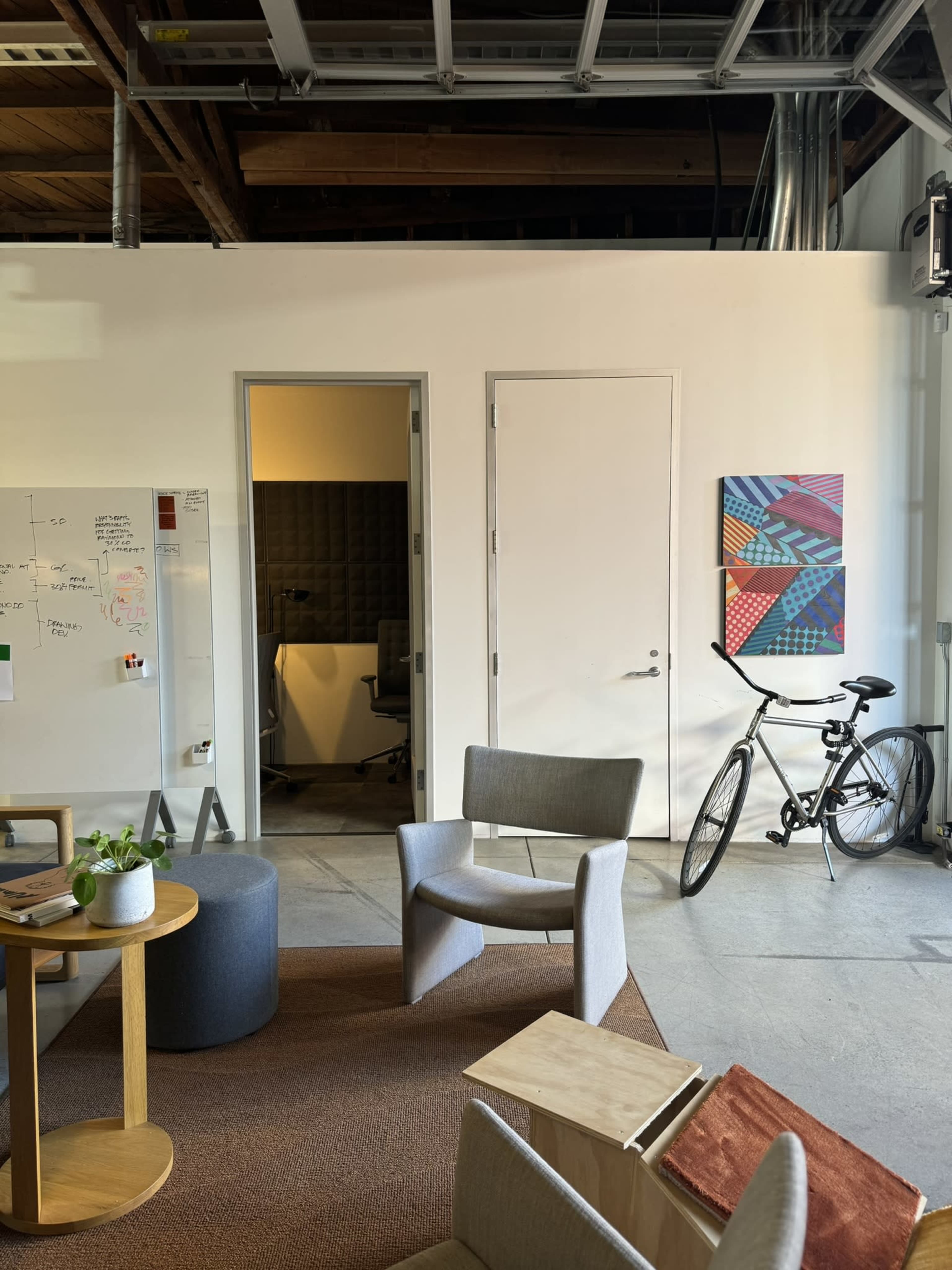 An office space featuring a seating area with modern chairs, a wooden table, a bicycle, and a whiteboard on the wall.