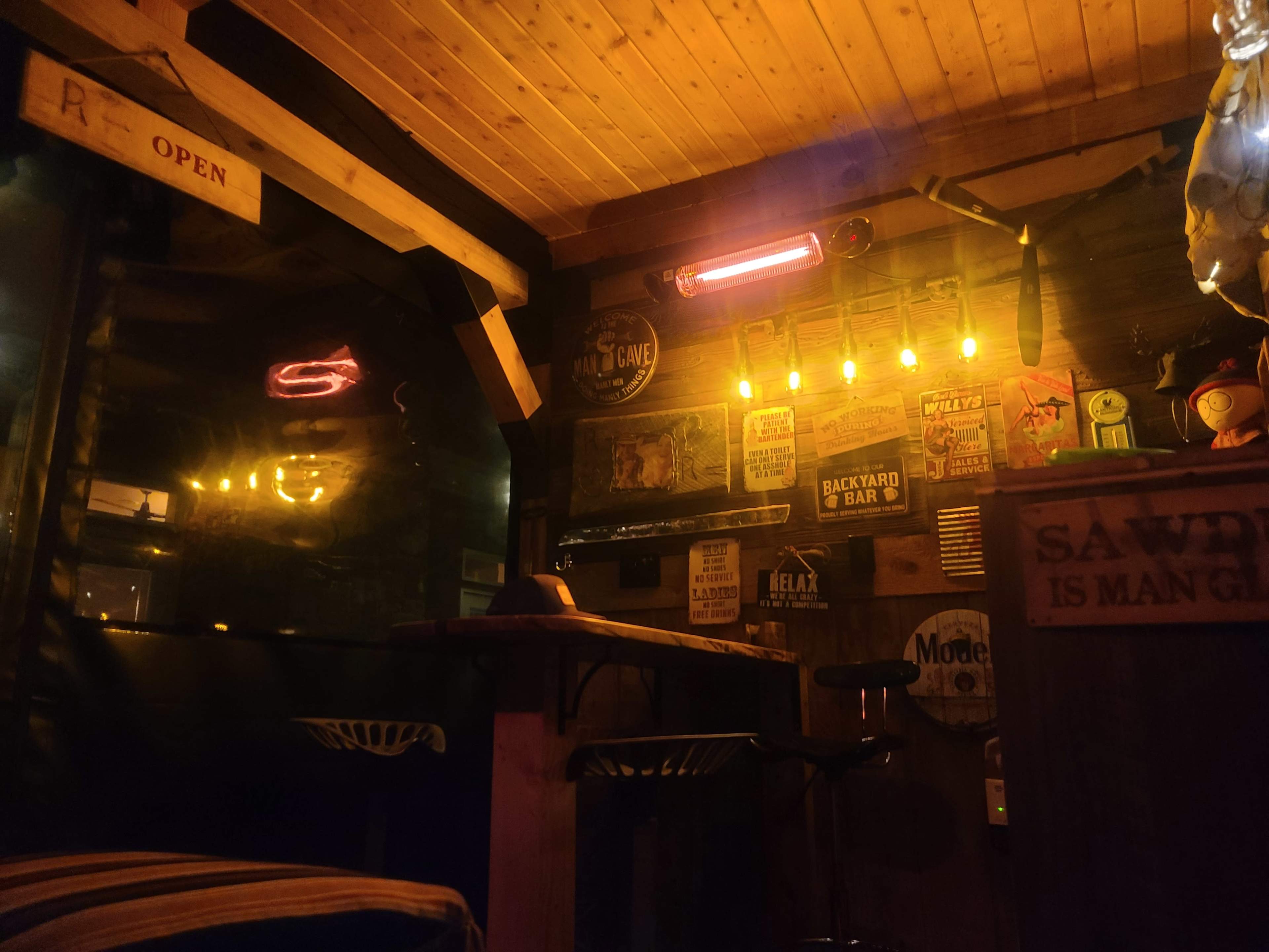 A dimly lit bar interior with wooden paneling, a counter, and various signs on the walls.