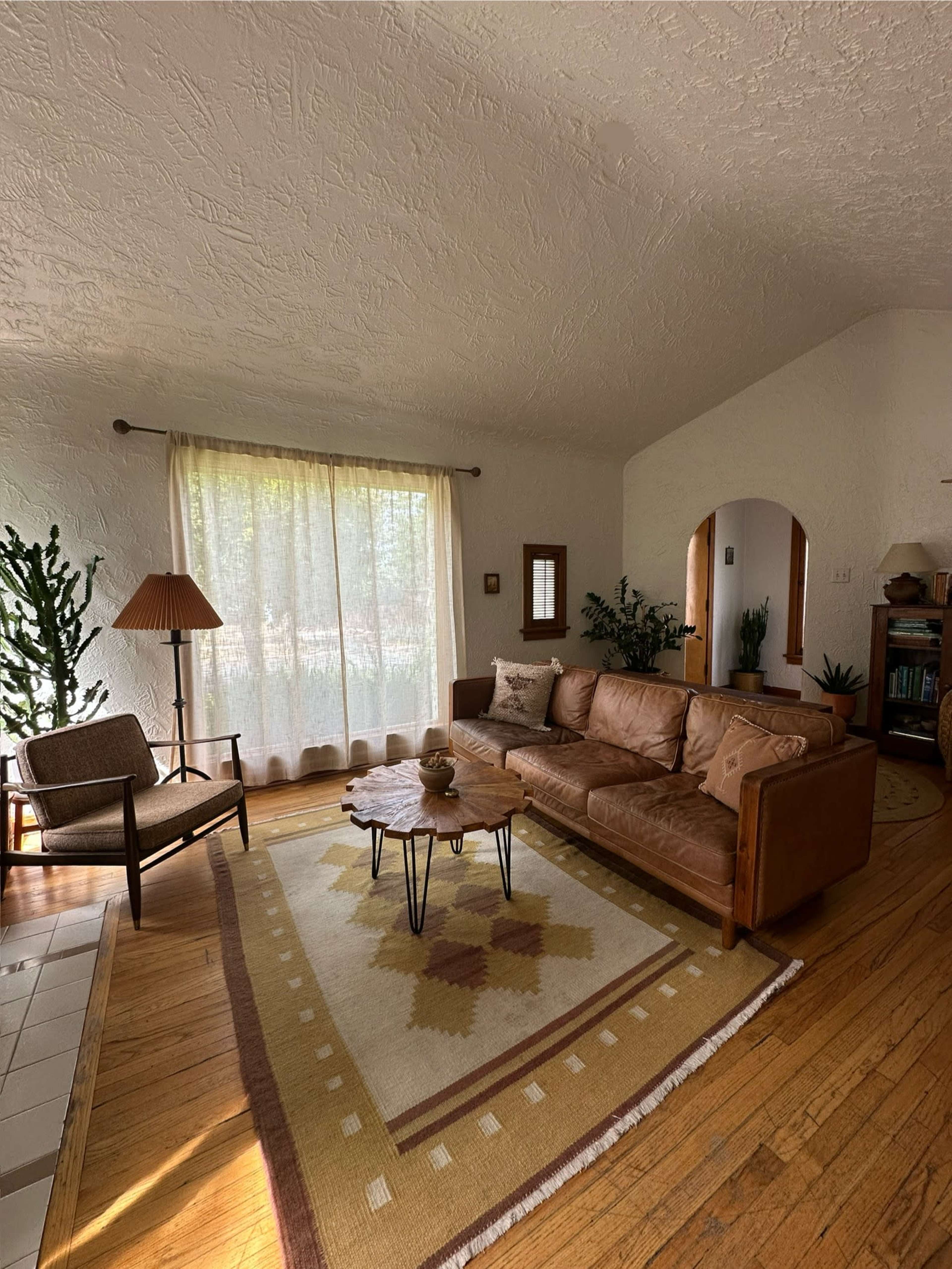 The image shows a living room with a brown leather sofa, a wooden coffee table, and a chair, illuminated by natural light from a large window.