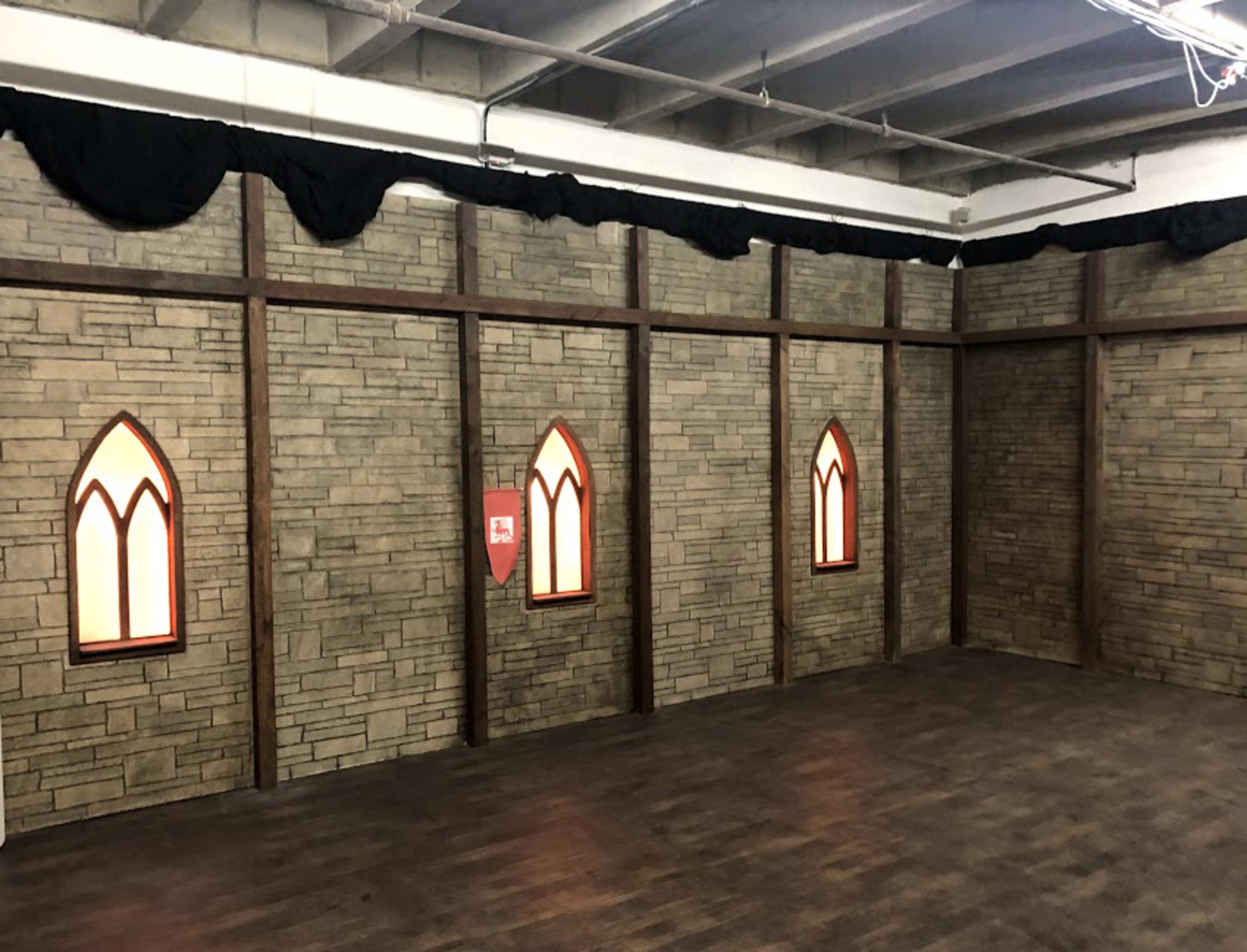 An interior room with stone-patterned walls, decorative windows resembling stained glass, and wooden beams.