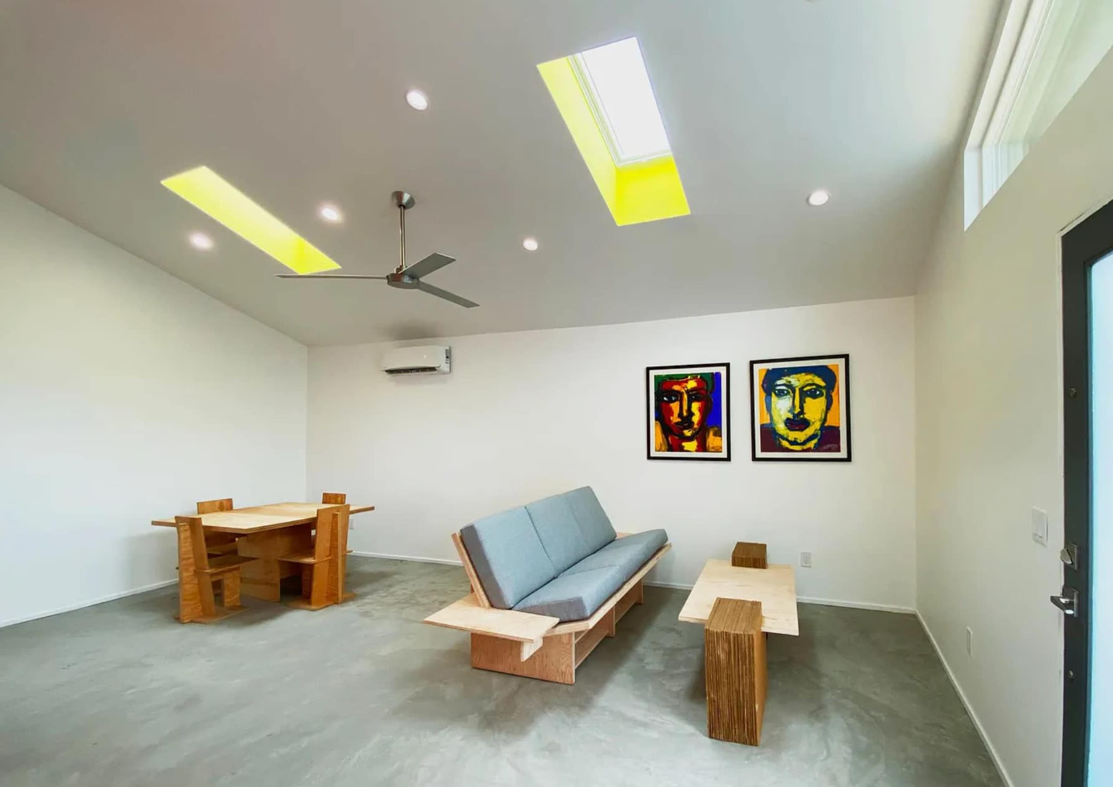 A modern interior space with a gray sofa, wooden furniture, and vibrant framed artwork on the walls.
