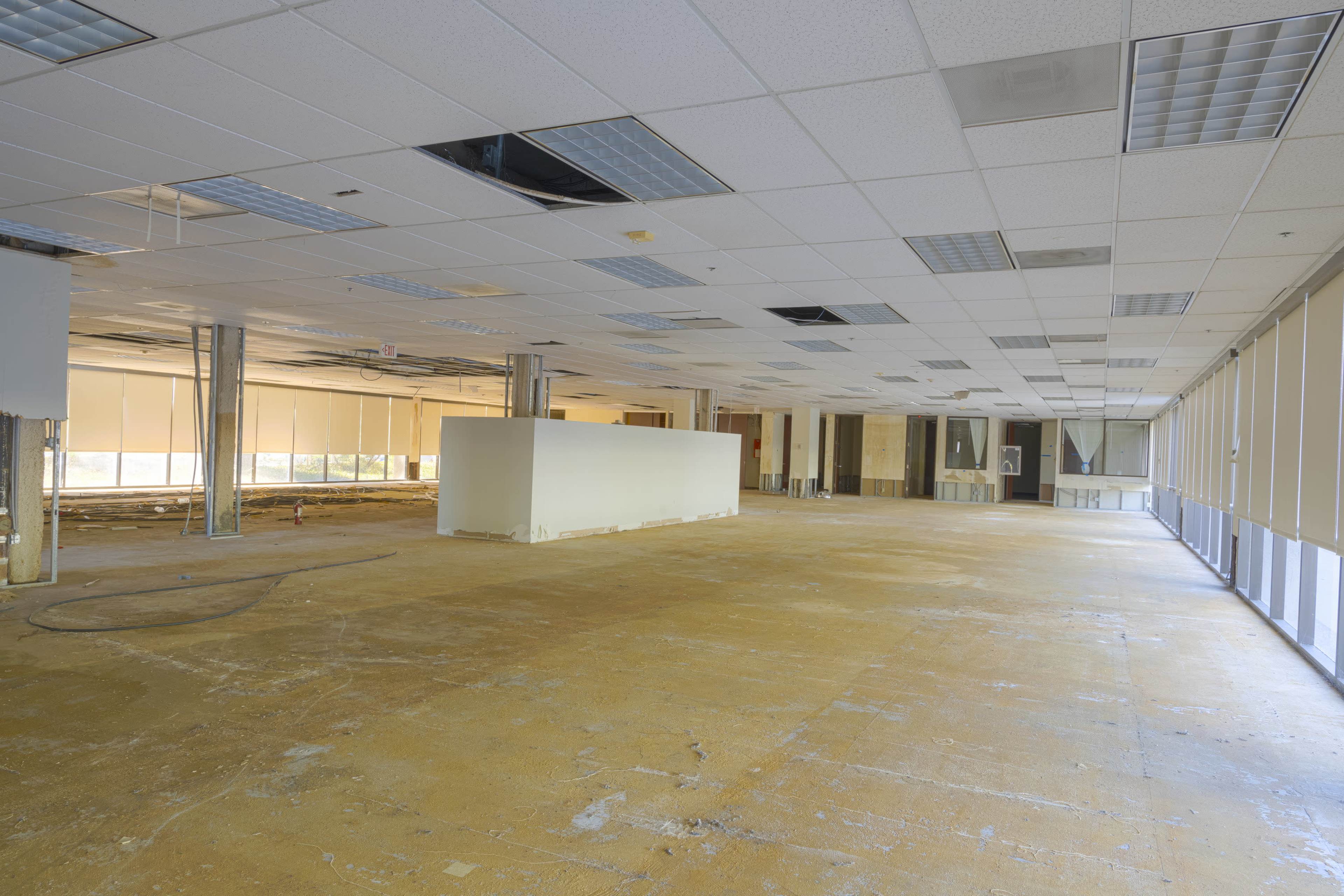 An empty office space with bare concrete floors, exposed columns, and partially removed ceiling panels.
