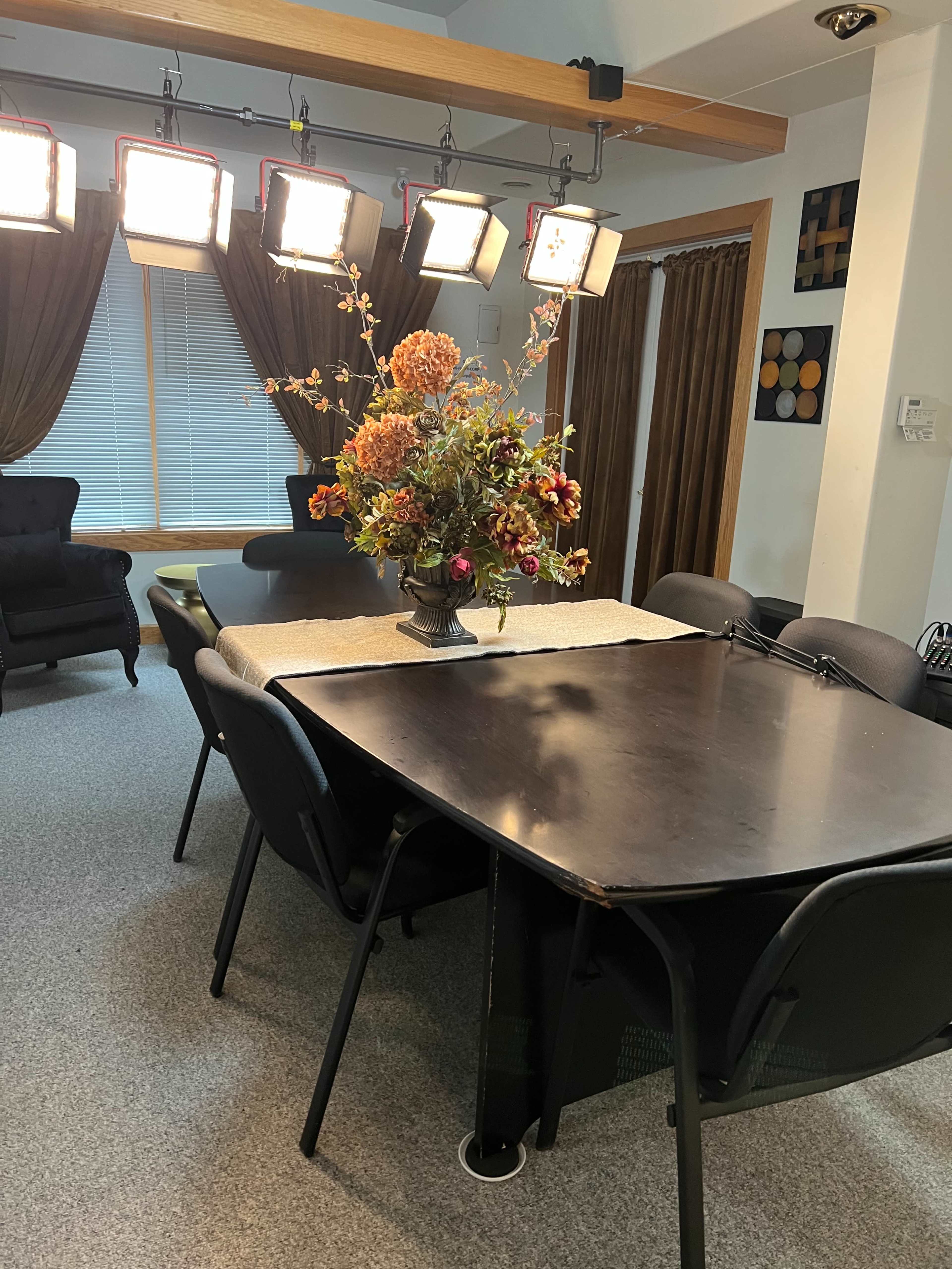 A dining table with a decorative flower arrangement is centered in a room featuring soft lighting and dark curtains.