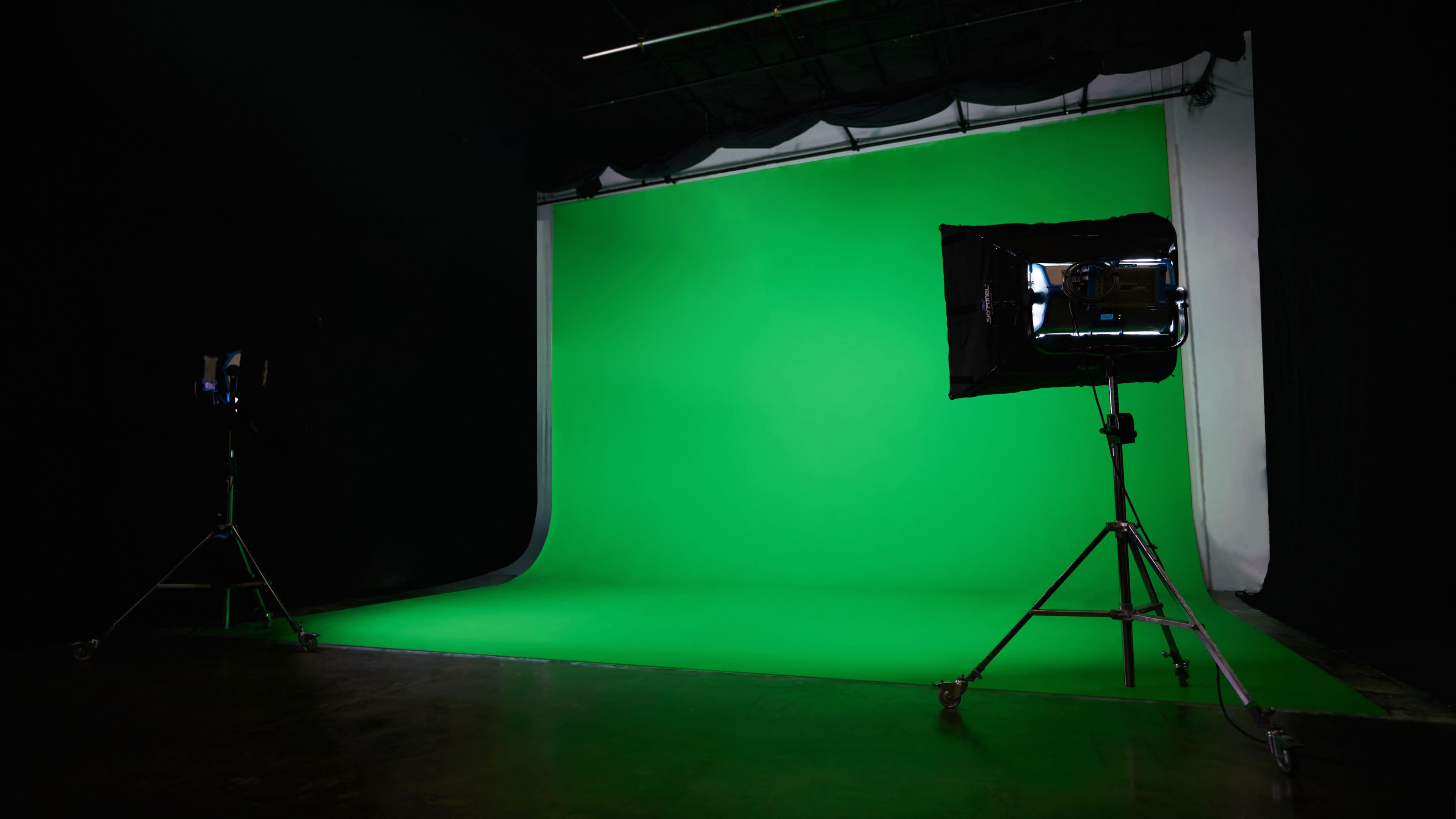A photography studio with a green screen backdrop, accompanied by professional lighting on stands.